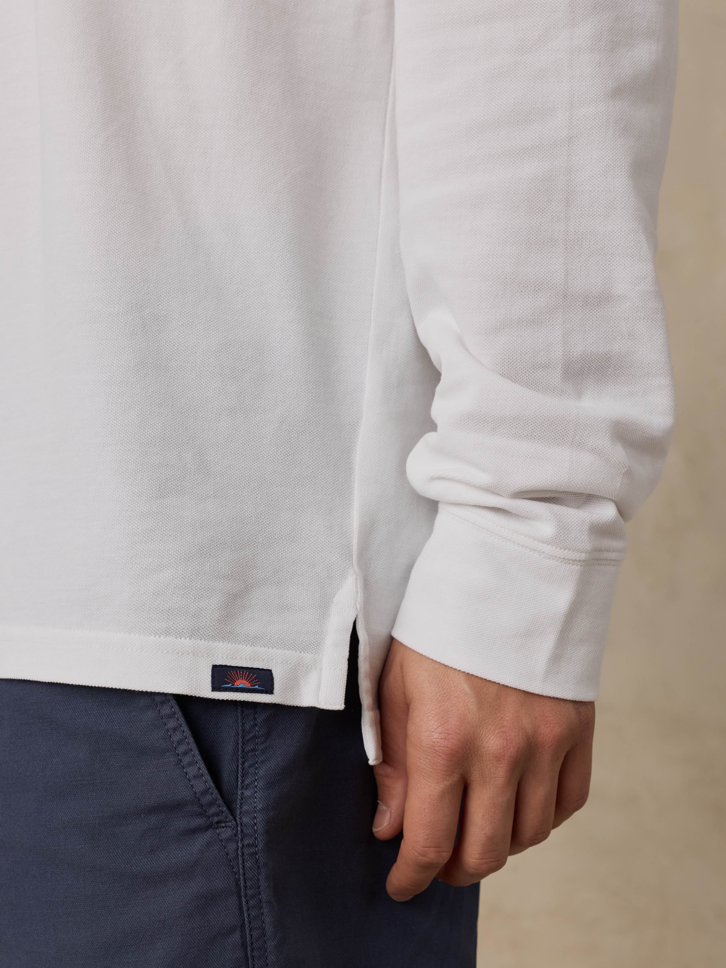 Close-up of a man wearing a white long-sleeve polo with a Faherty brand logo and navy shorts
