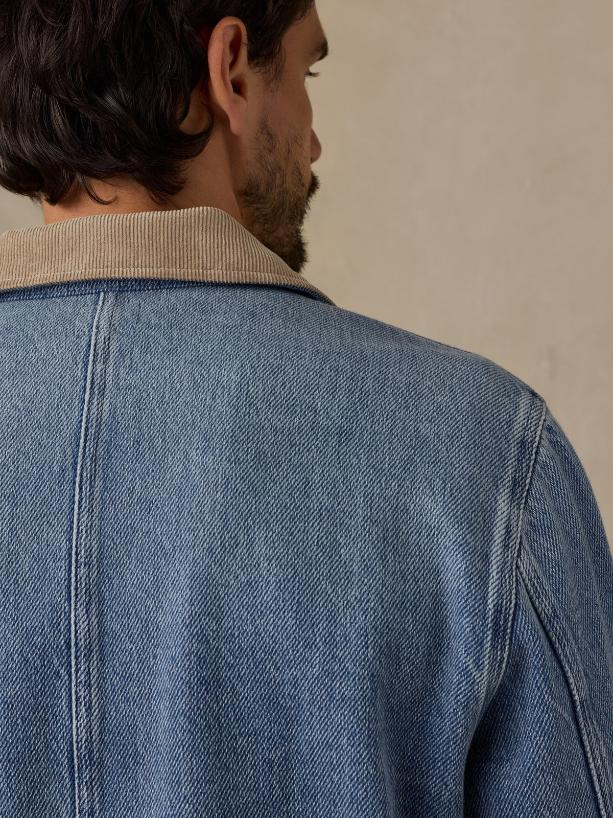 Man wearing a blue denim jacket with tan corduroy collar against a beige background, image 5 of 6
