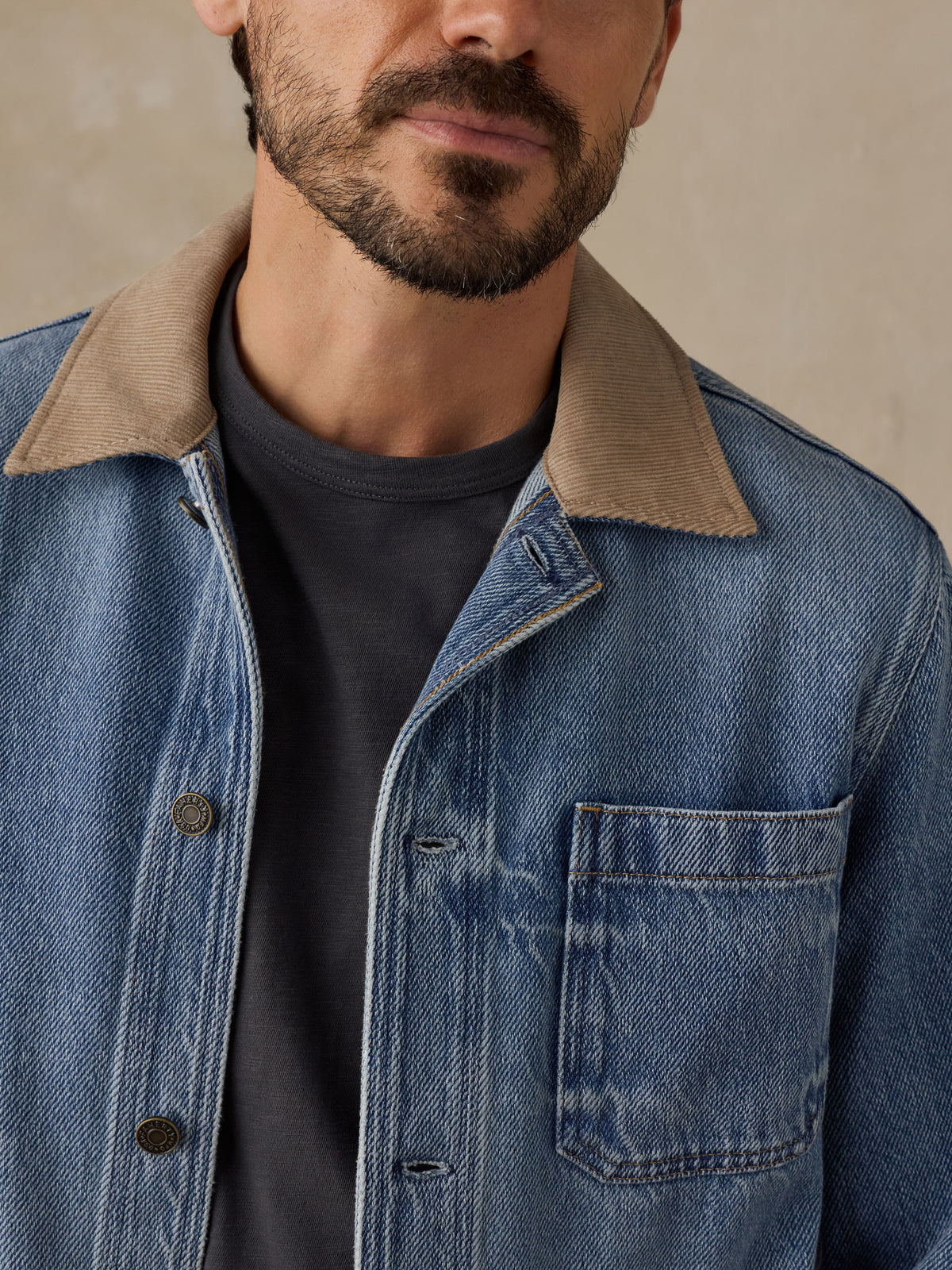 Man wearing a blue denim jacket with tan corduroy collar and a blue t-shirt against a beige background, image 2 of 6
