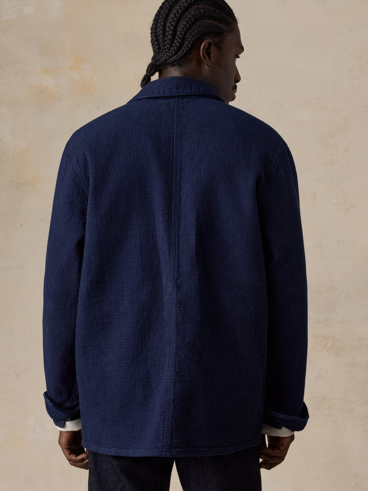 A man viewed from behind wearing a blue jacket and blue jeans, image 2 of 6