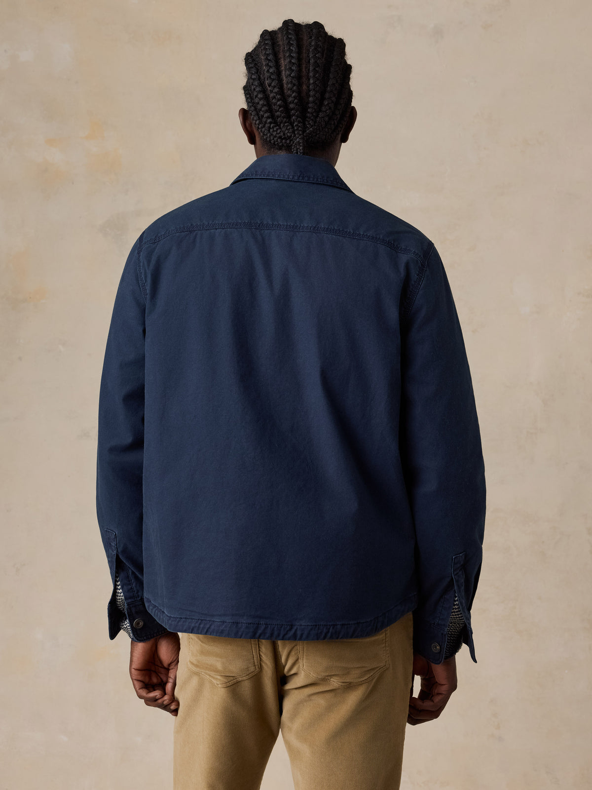 A man viewed from behind wearing a blue jacket and tan corduroy pants, image 3 of 5