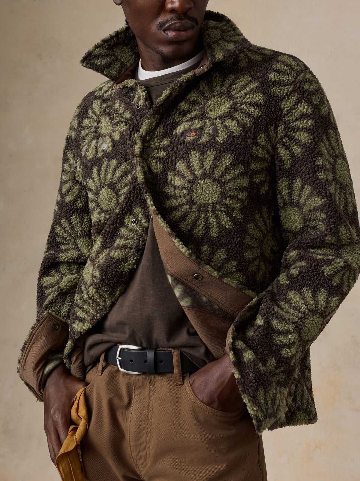 A man wearing a floral fleece jacket over a brown tee and brown pants, image 6 of 7