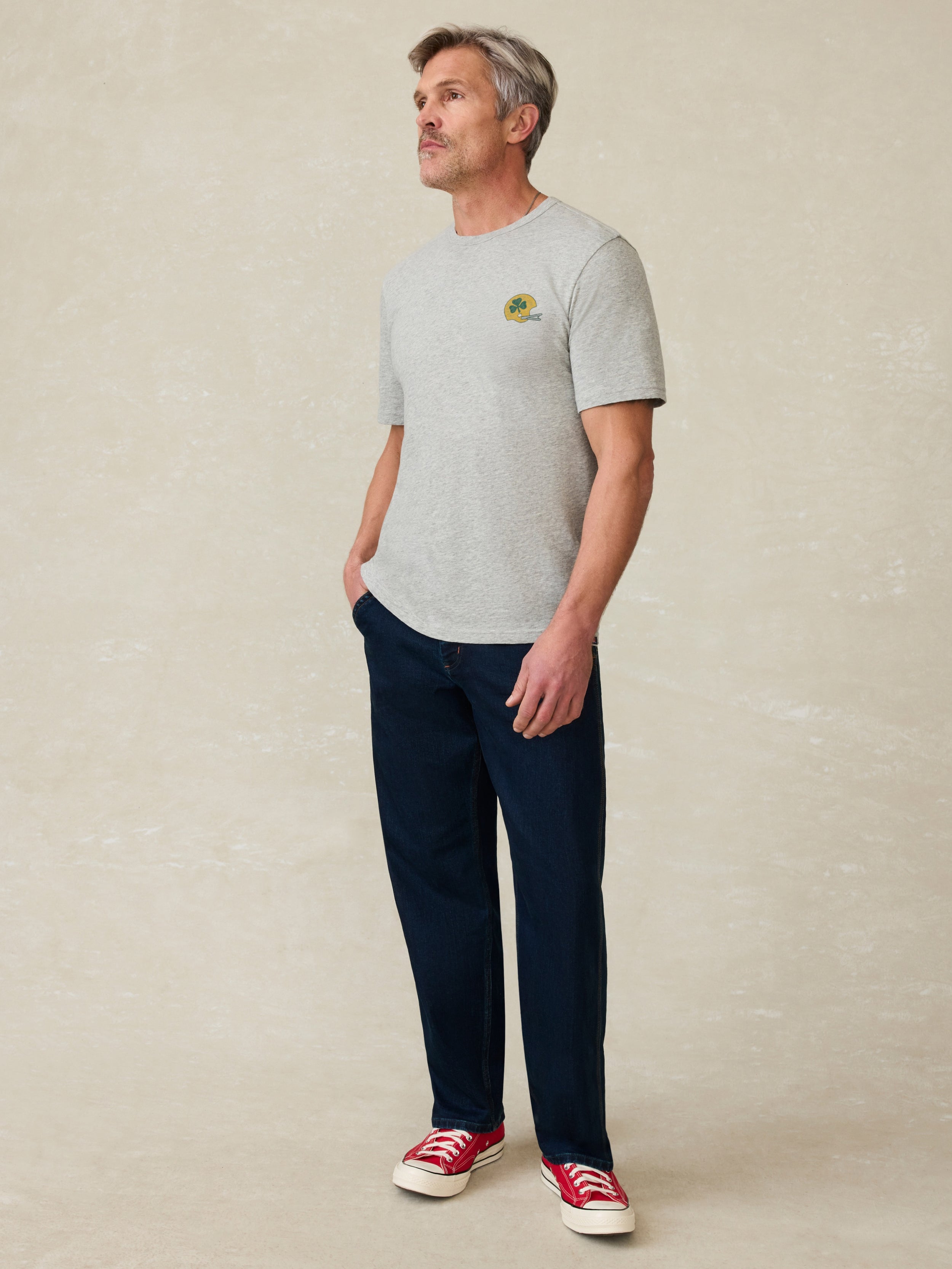 Man wearing a gray t-shirt with 'Notre Dame Football' graphic on the chest against a beige background