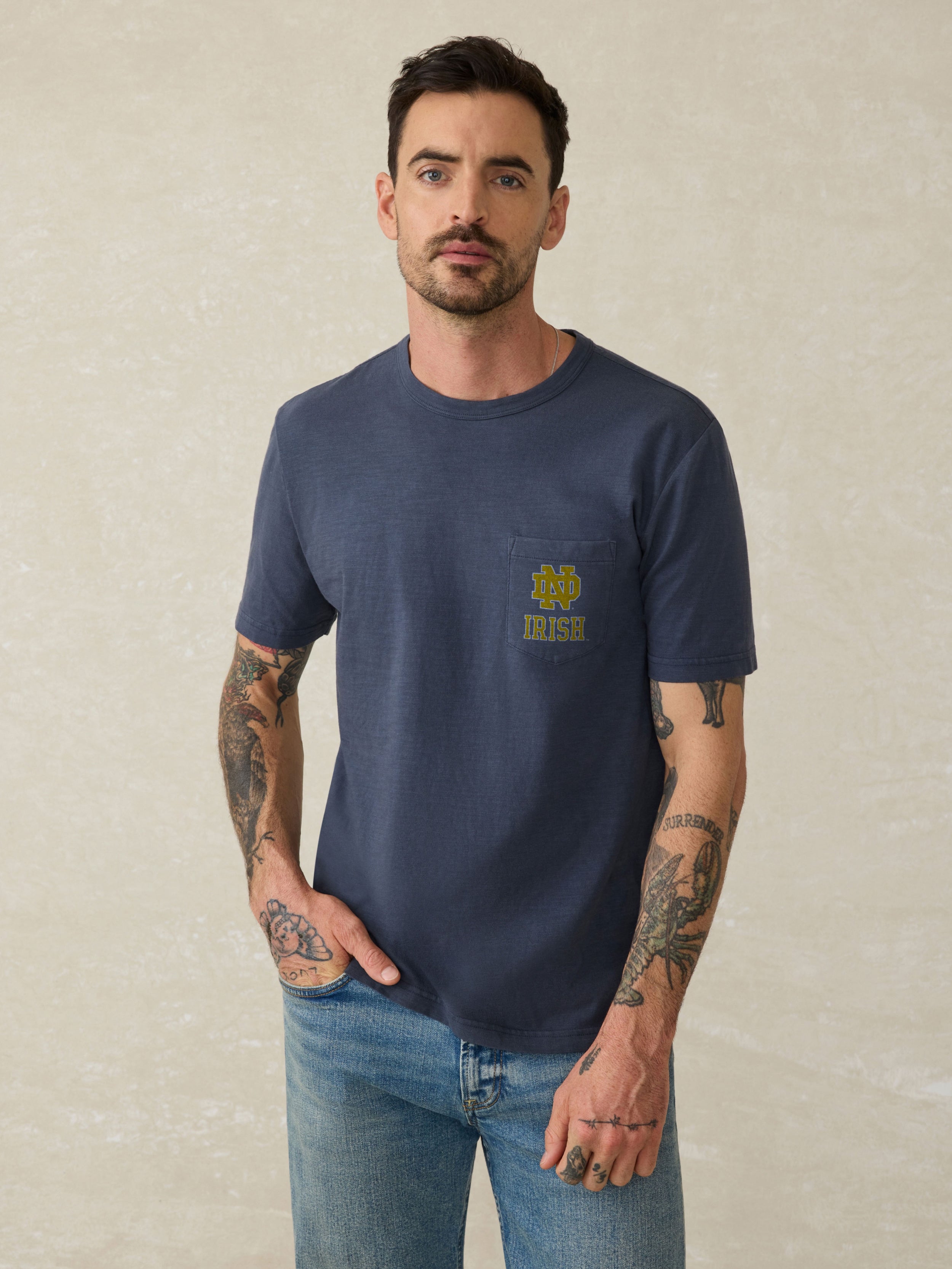 Man wearing a navy blue t-shirt with a Notre Dame logo on the chest against a beige background