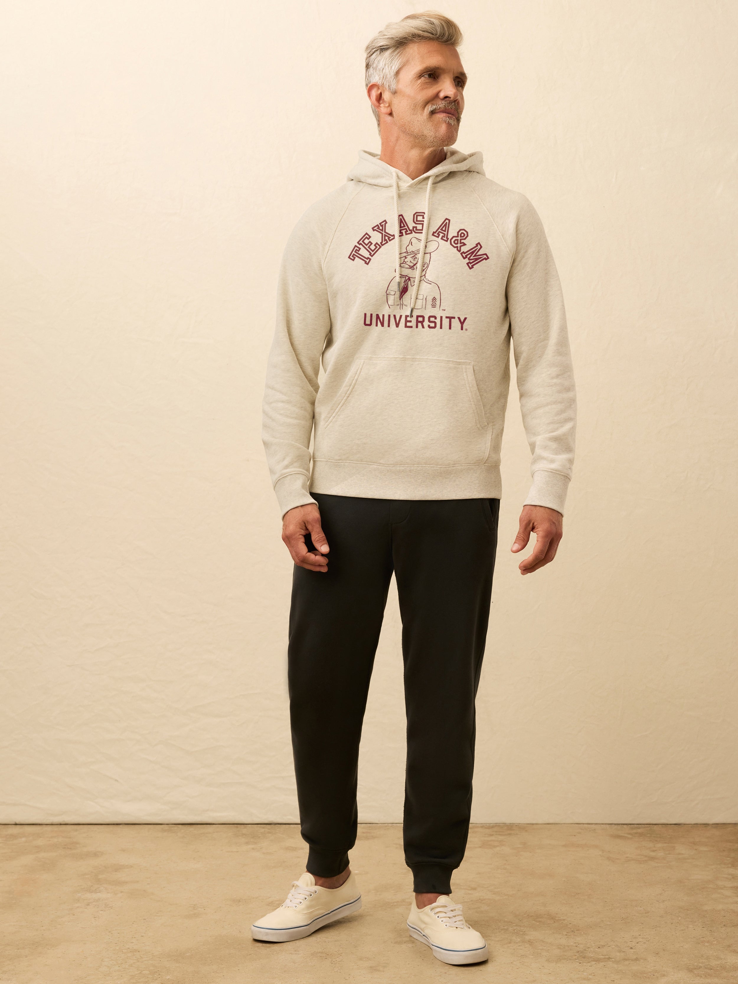 Man wearing an ivory hooded sweatshirt with Texas A&M graphic at the front against a beige background