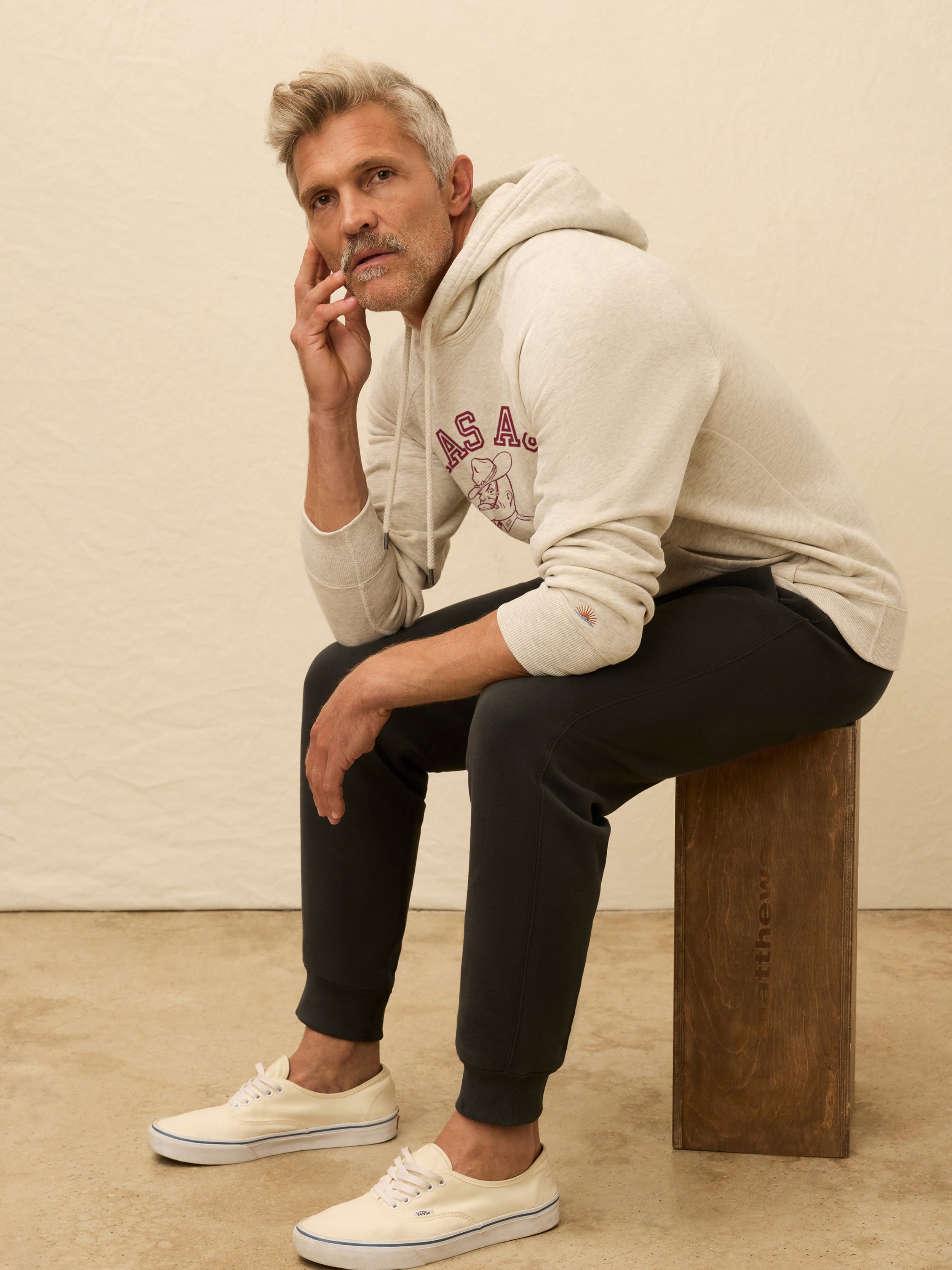 Man wearing an ivory hooded sweatshirt with Texas A&M graphic at the front against a beige background