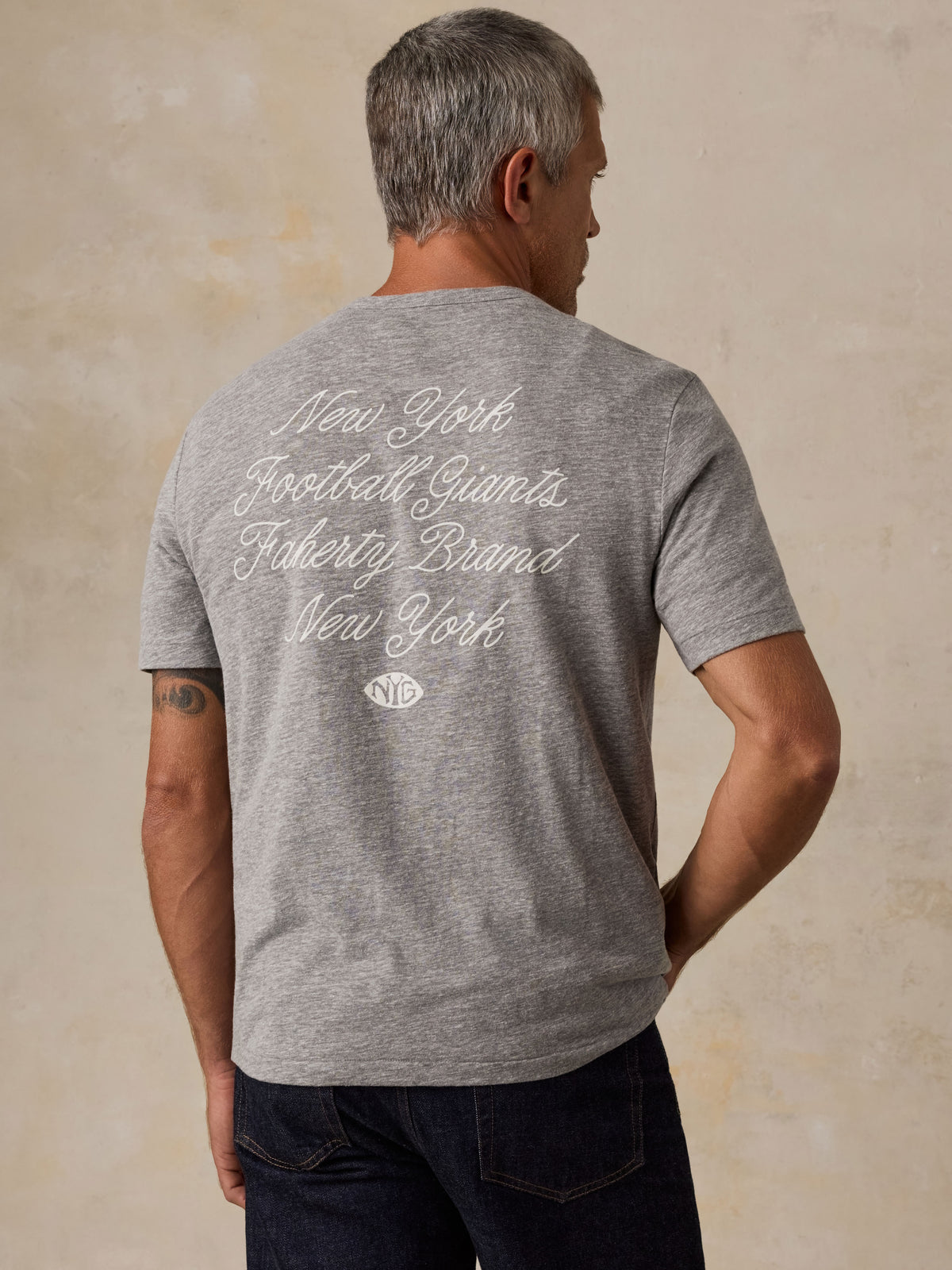 A man viewed from behind wearing a grey NY Giants t-shirt with blue jeans, image 2 of 6