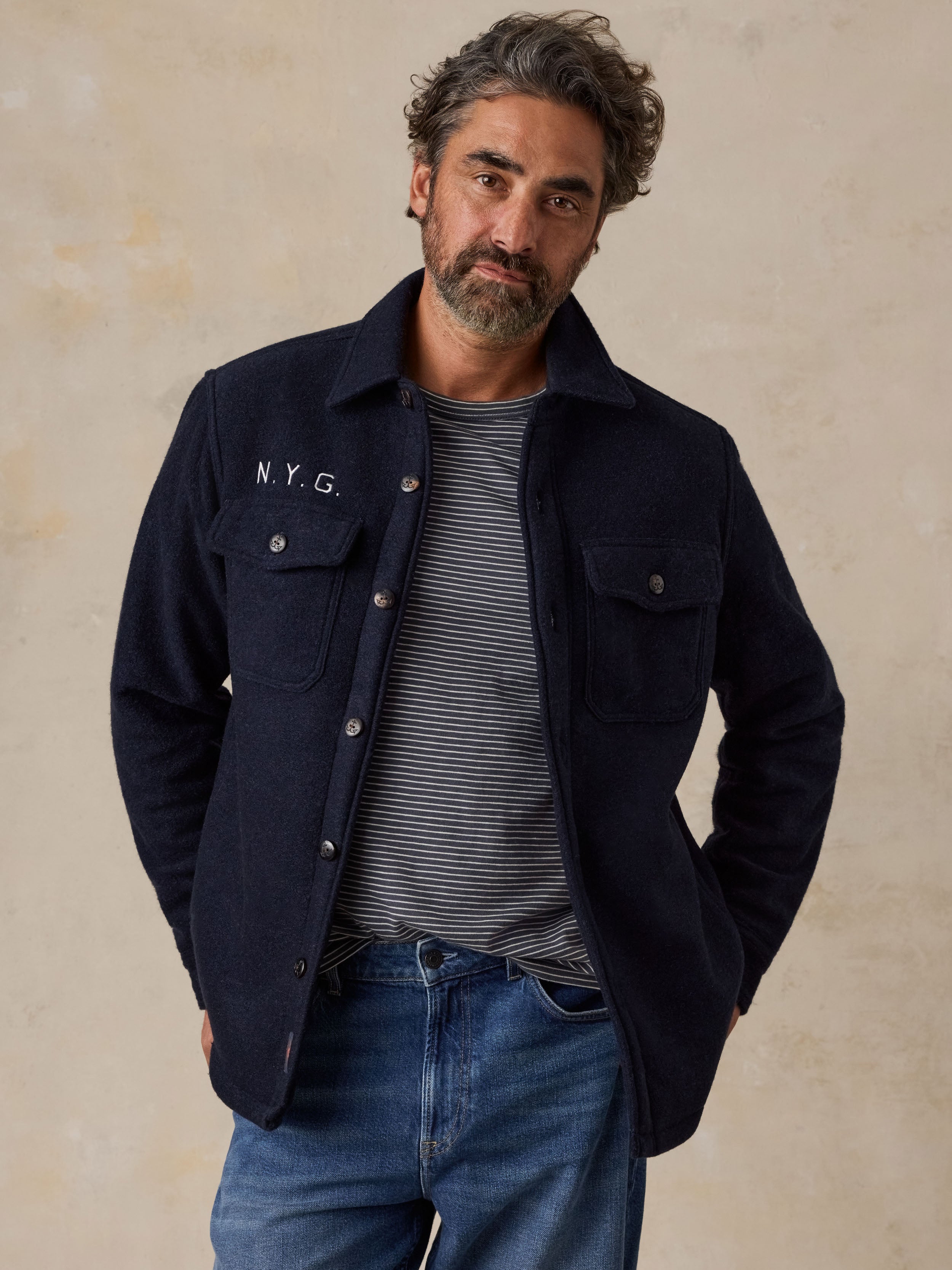 A man wearing a blue NY Giants jacket over a striped tee and blue jeans