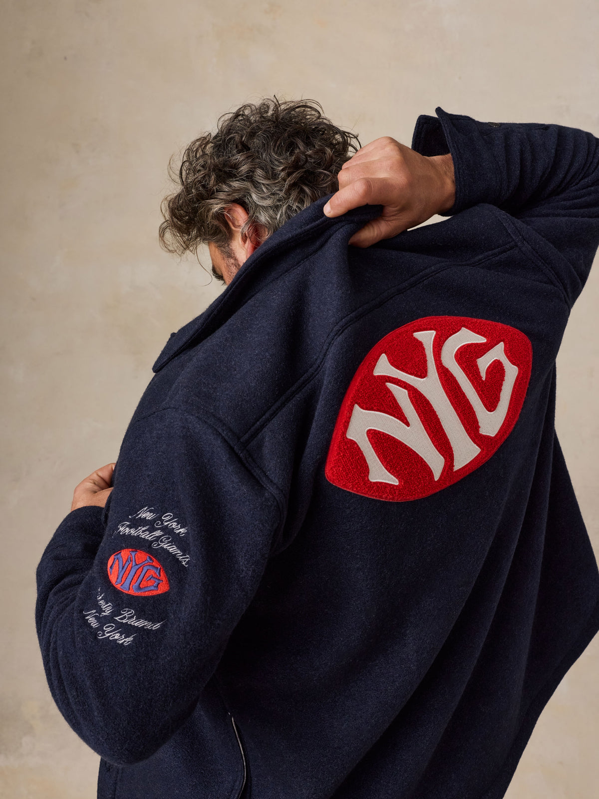 A man viewed from behind wearing a blue NY Giants jacket, image 2 of 5