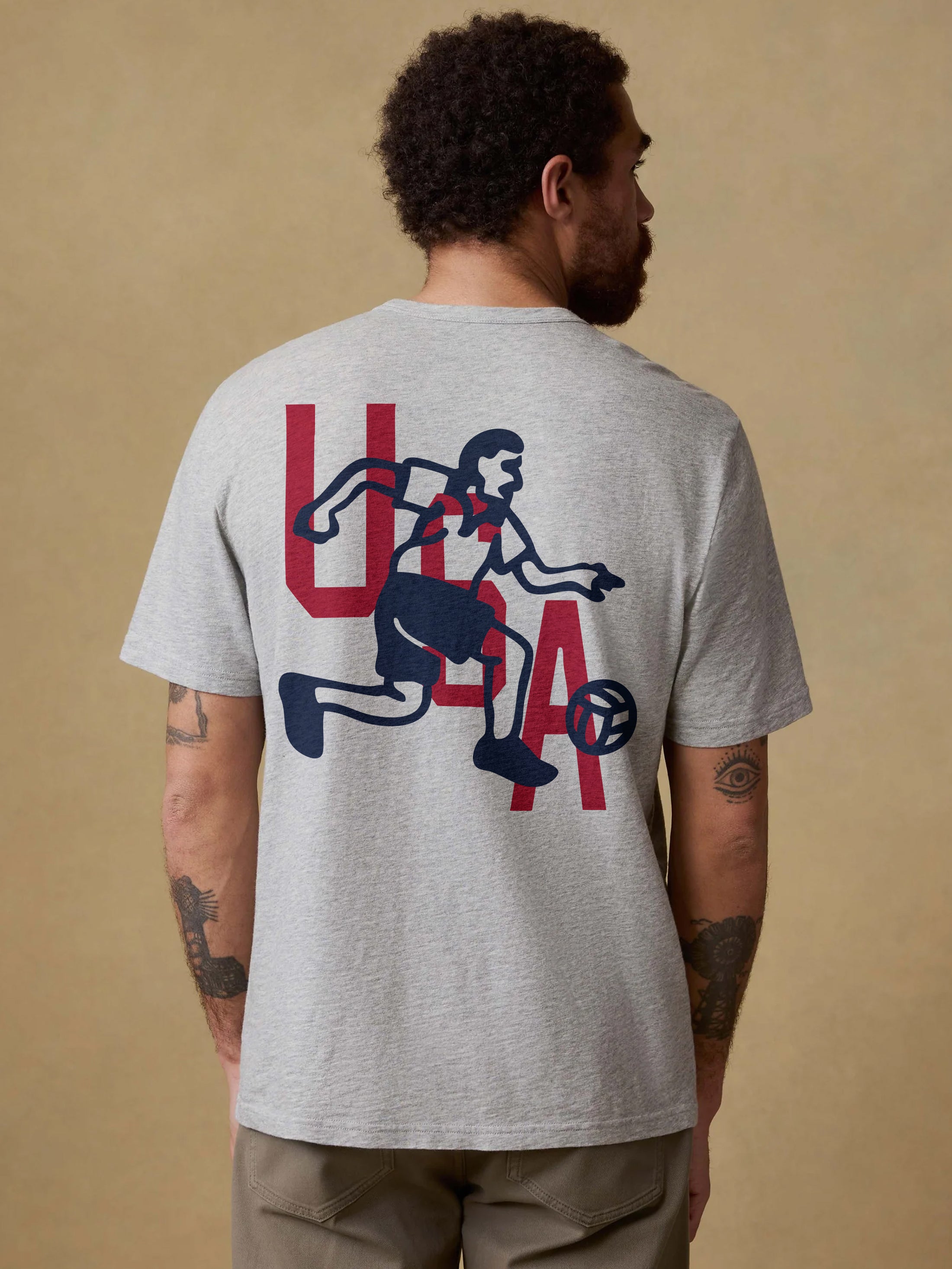 Man wearing a gray t-shirt with a graphic design on the back against a beige background