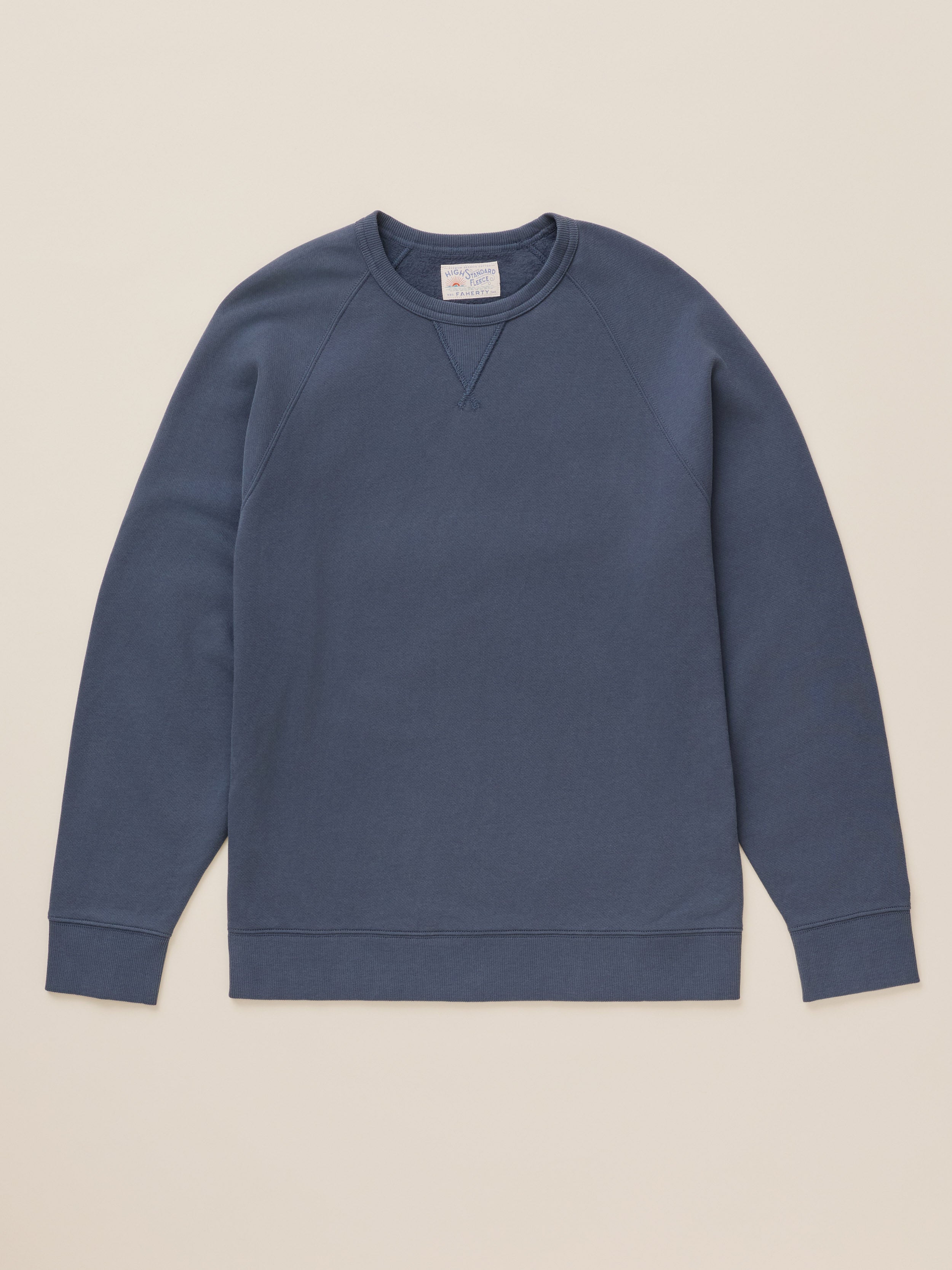 A slate blue crewneck sweatshirt with raglan sleeves, laid flat against a solid beige background.