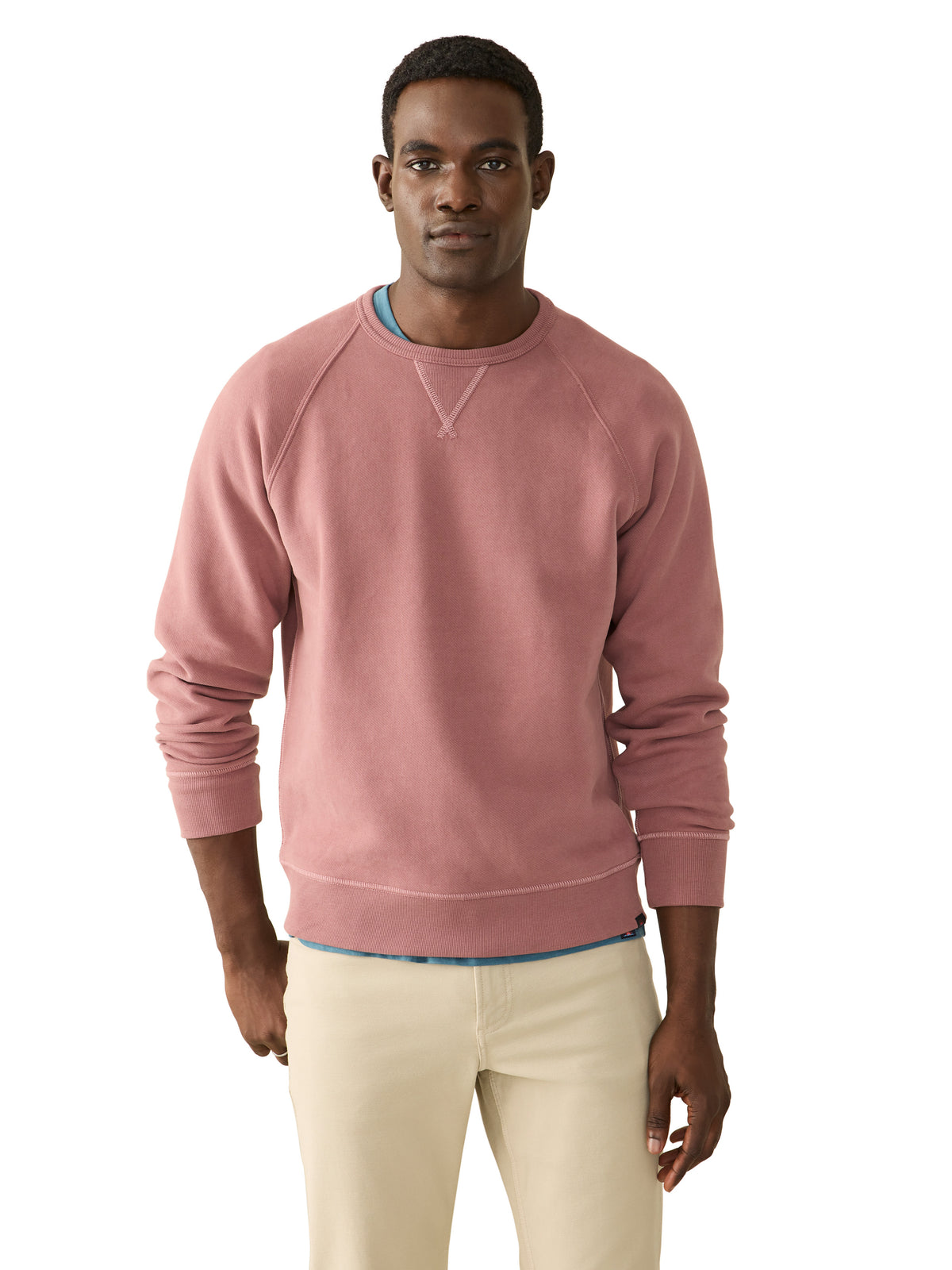A man wearing a pink crewneck and beige pants, image 1 of 3
