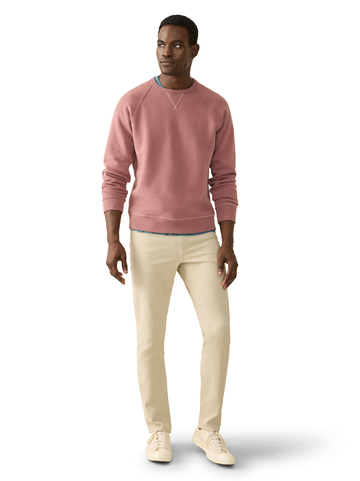 A man wearing a pink crewneck, beige pants, and sneakers, image 2 of 3