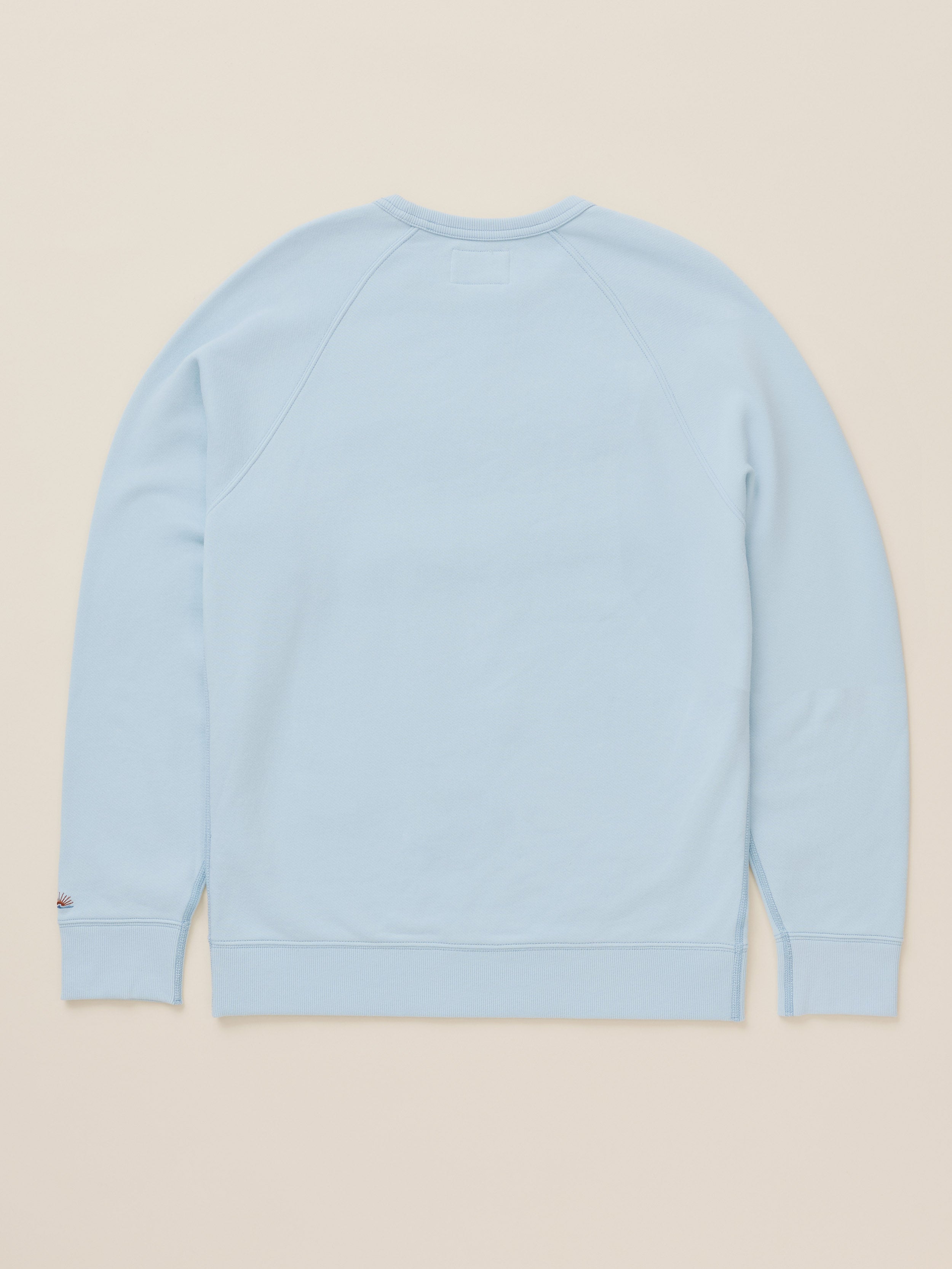 A light blue crewneck sweatshirt shown from the back, laid flat against a solid beige background.