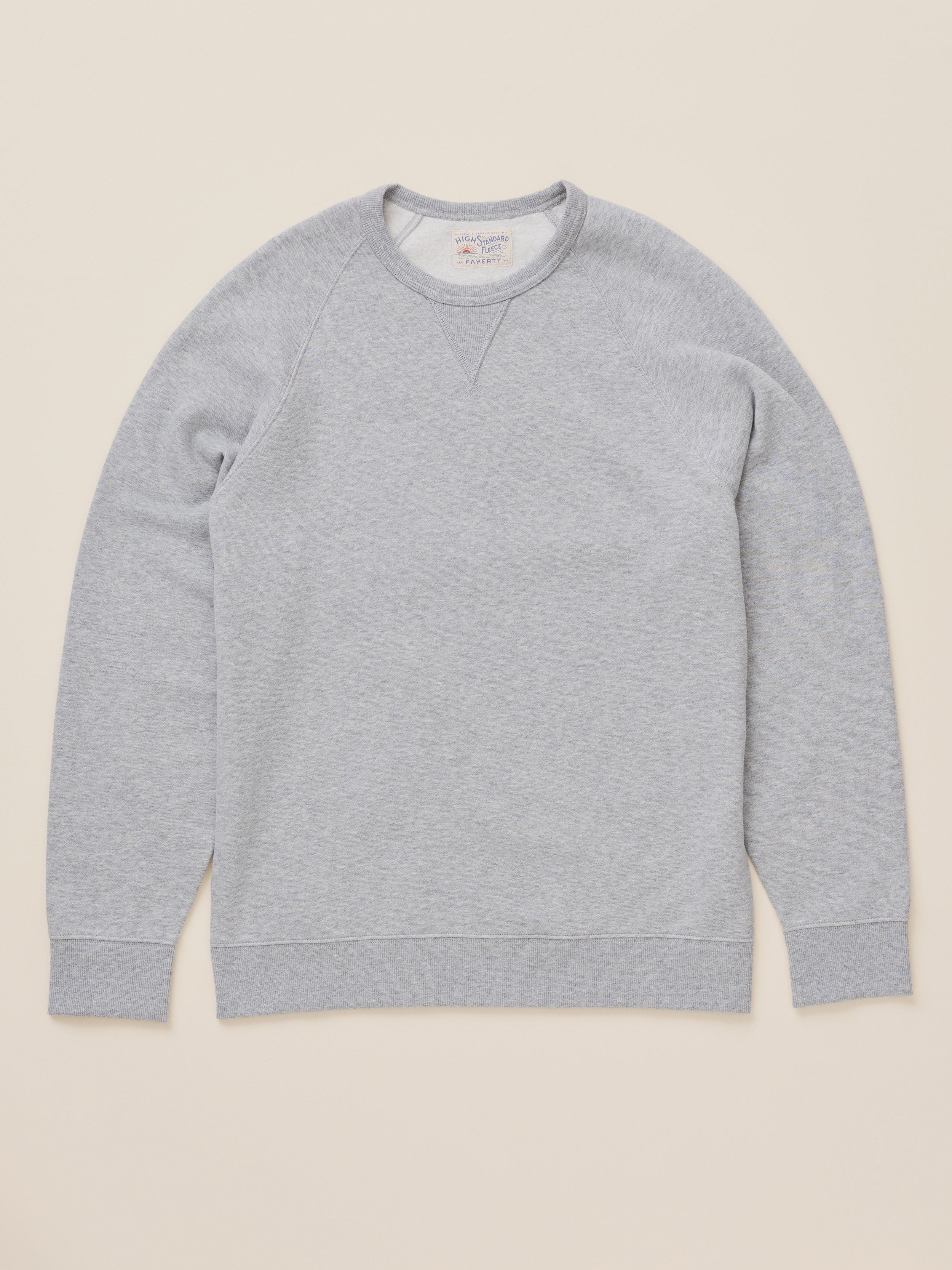 A light gray heather crewneck sweatshirt with raglan sleeves, laid flat against a solid beige background.