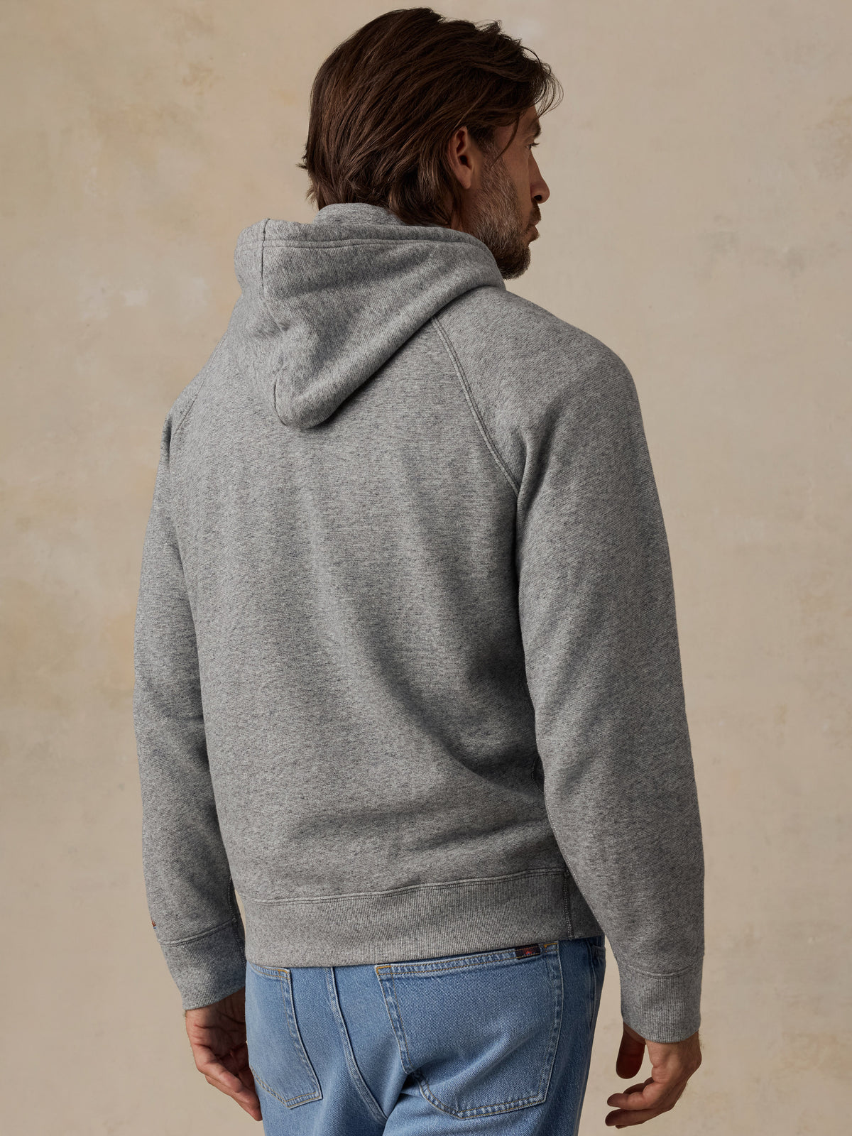 A man viewed from behind wearing a heather gray pullover hoodie paired with blue jeans, image 4 of 7