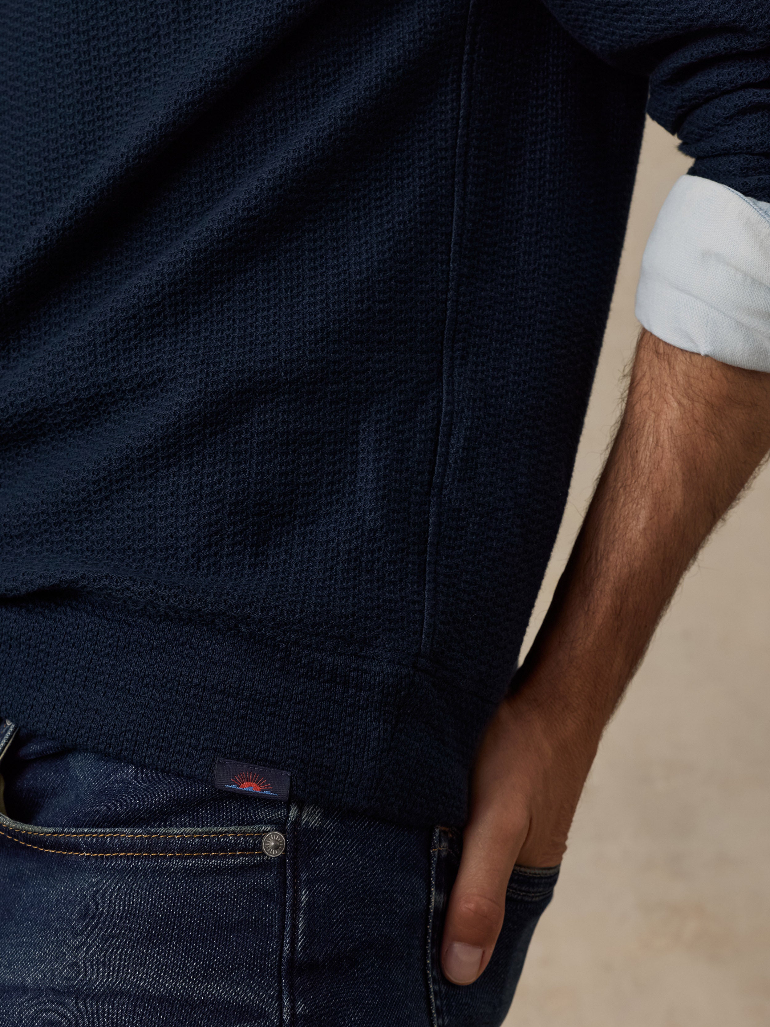 Close-up of a man wearing a dark navy textured knit sweater with rolled-up sleeves, paired with dark blue jeans.