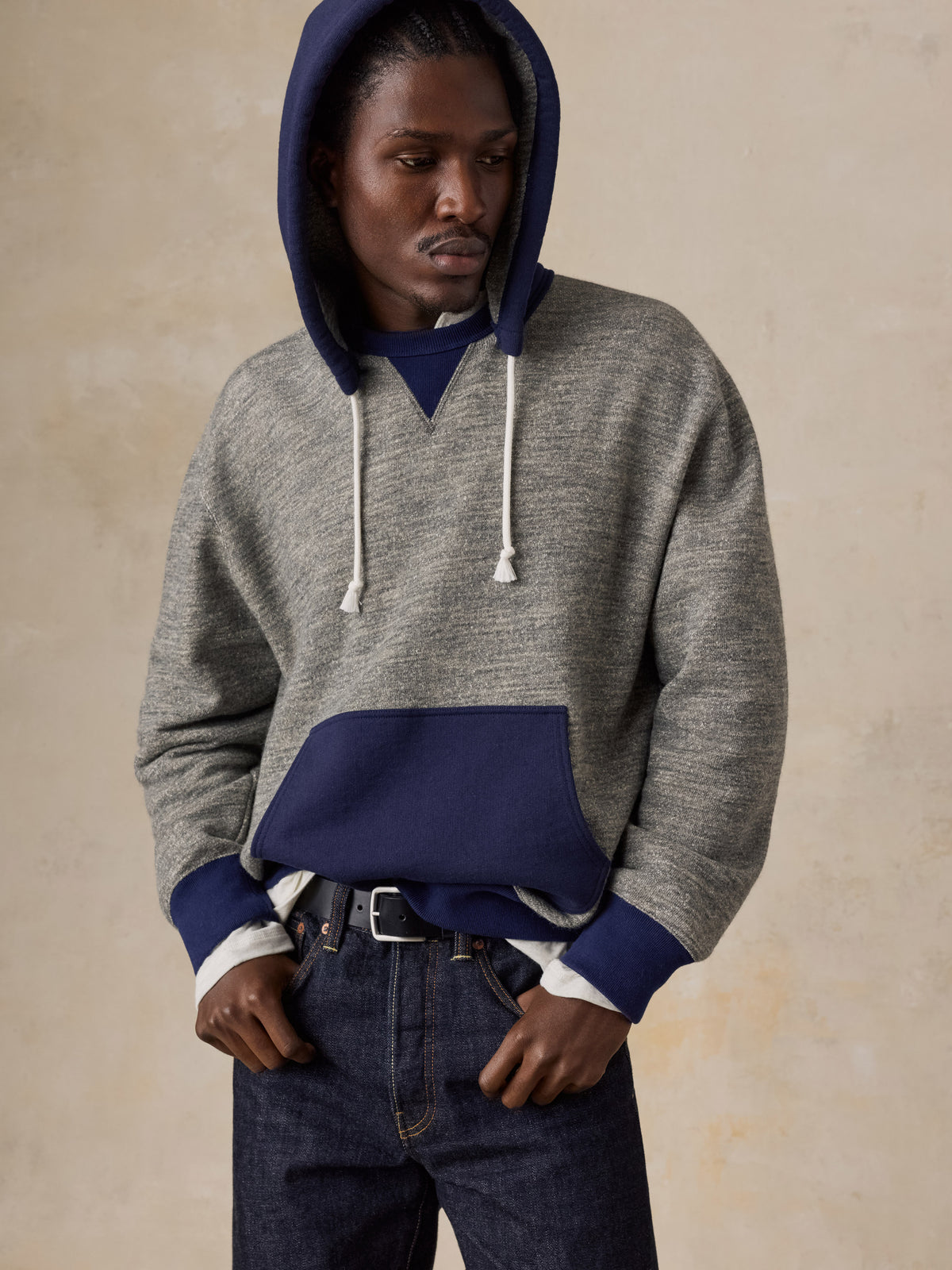 A man wearing a blue and grey hoodie with blue jeans, image 3 of 5