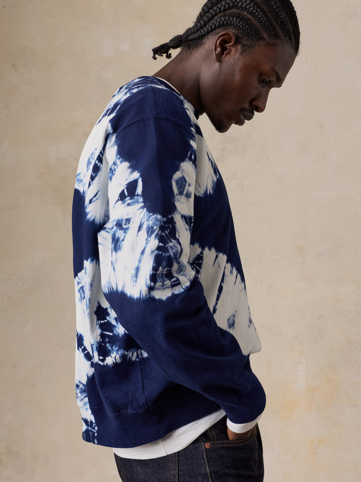 A man wearing a shibori dyed sweatshirt and blue jeans, image 3 of 6