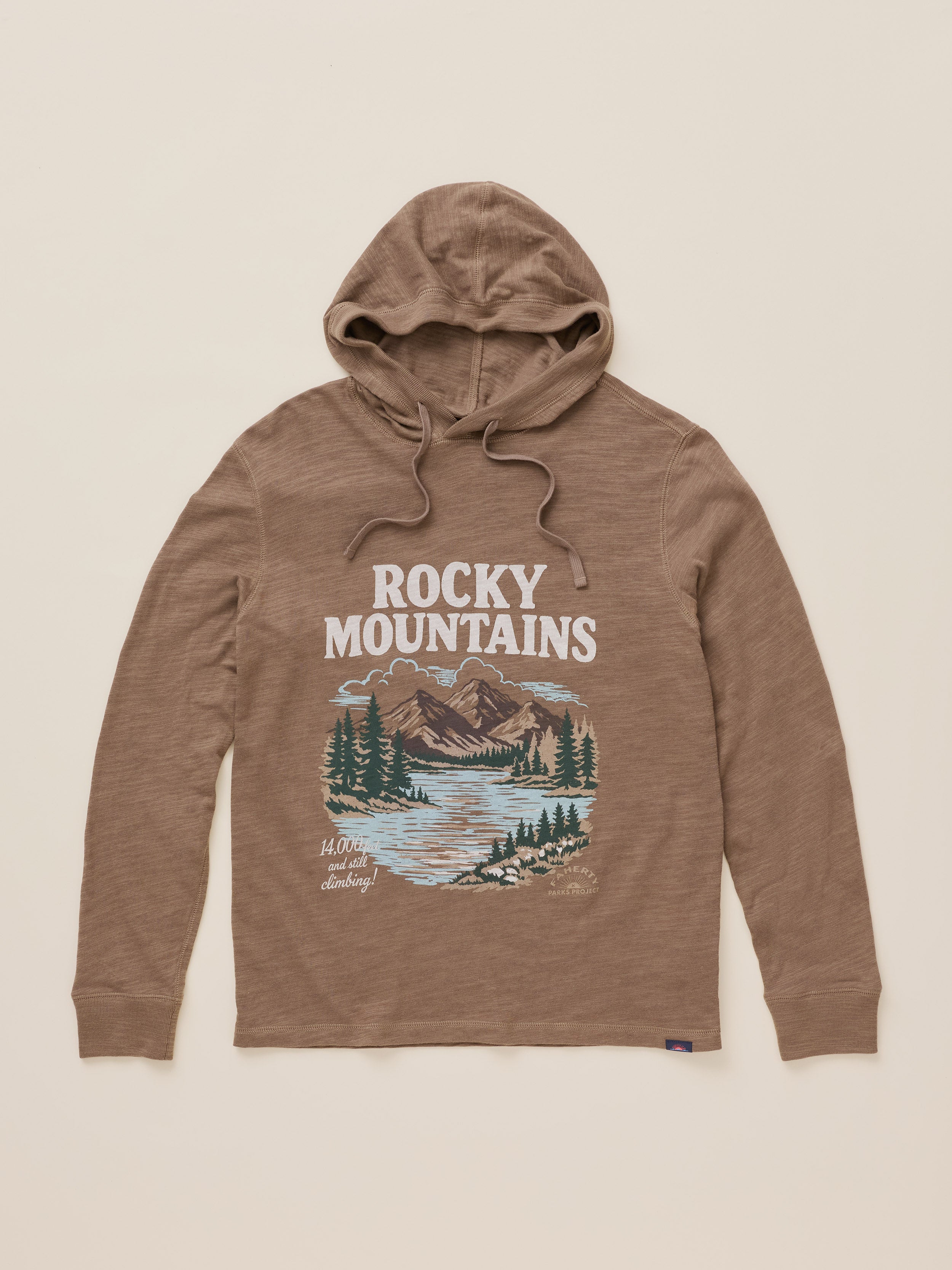 A brown heathered pullover hoodie with a drawstring hood and a front graphic print featuring the text 'ROCKY MOUNTAINS' above an illustration of a mountain landscape with trees and a river. The hoodie is laid flat against a solid light beige background.