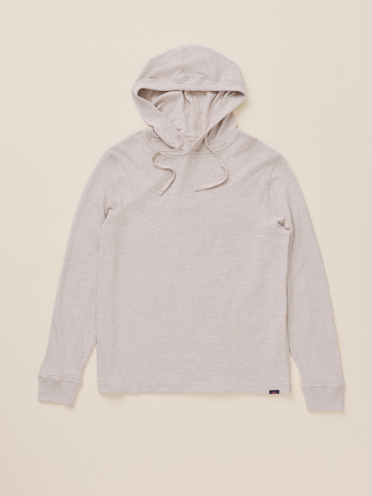 An oatmeal heather pullover hoodie with drawstrings, laid flat against a solid cream-colored background., image 6 of 7