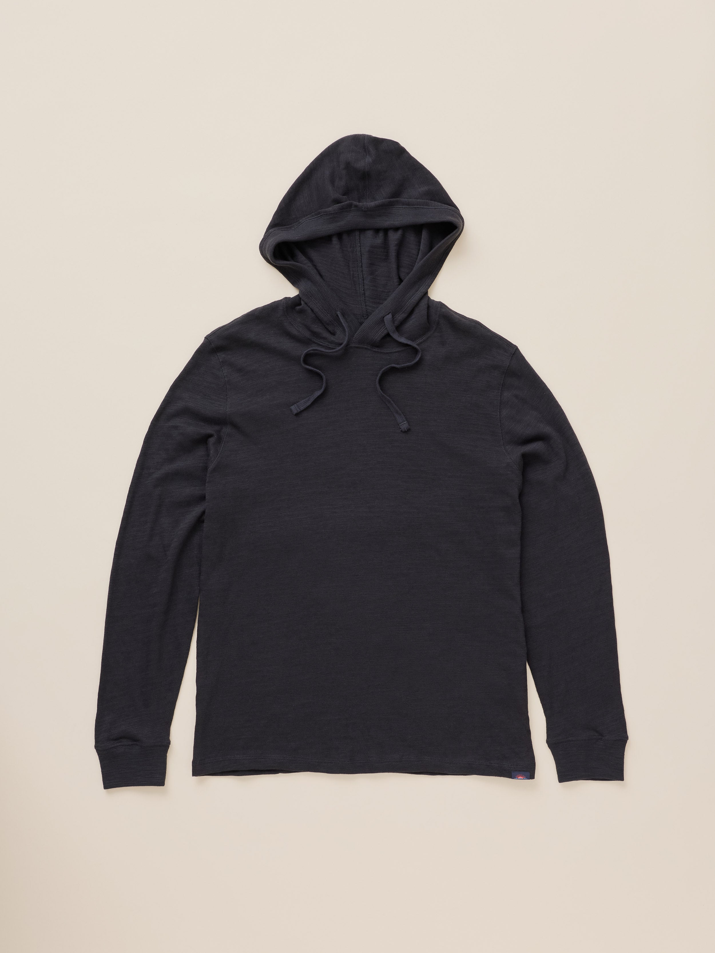 A black long-sleeve hoodie with a drawstring hood, laid flat against a light beige background.