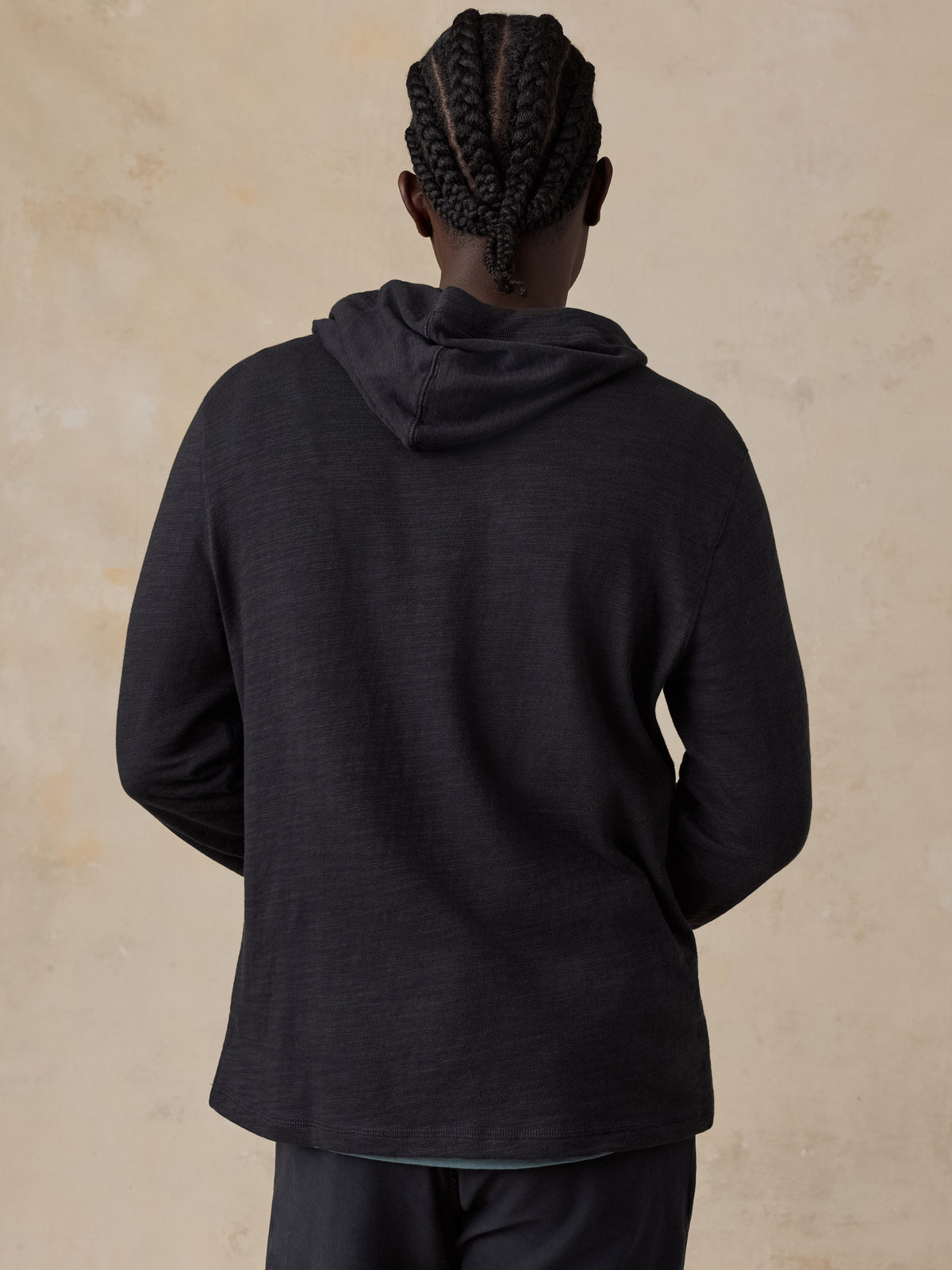 Man wearing a black hoodie and navy chino pants against a beige studio background, image 3 of 7
