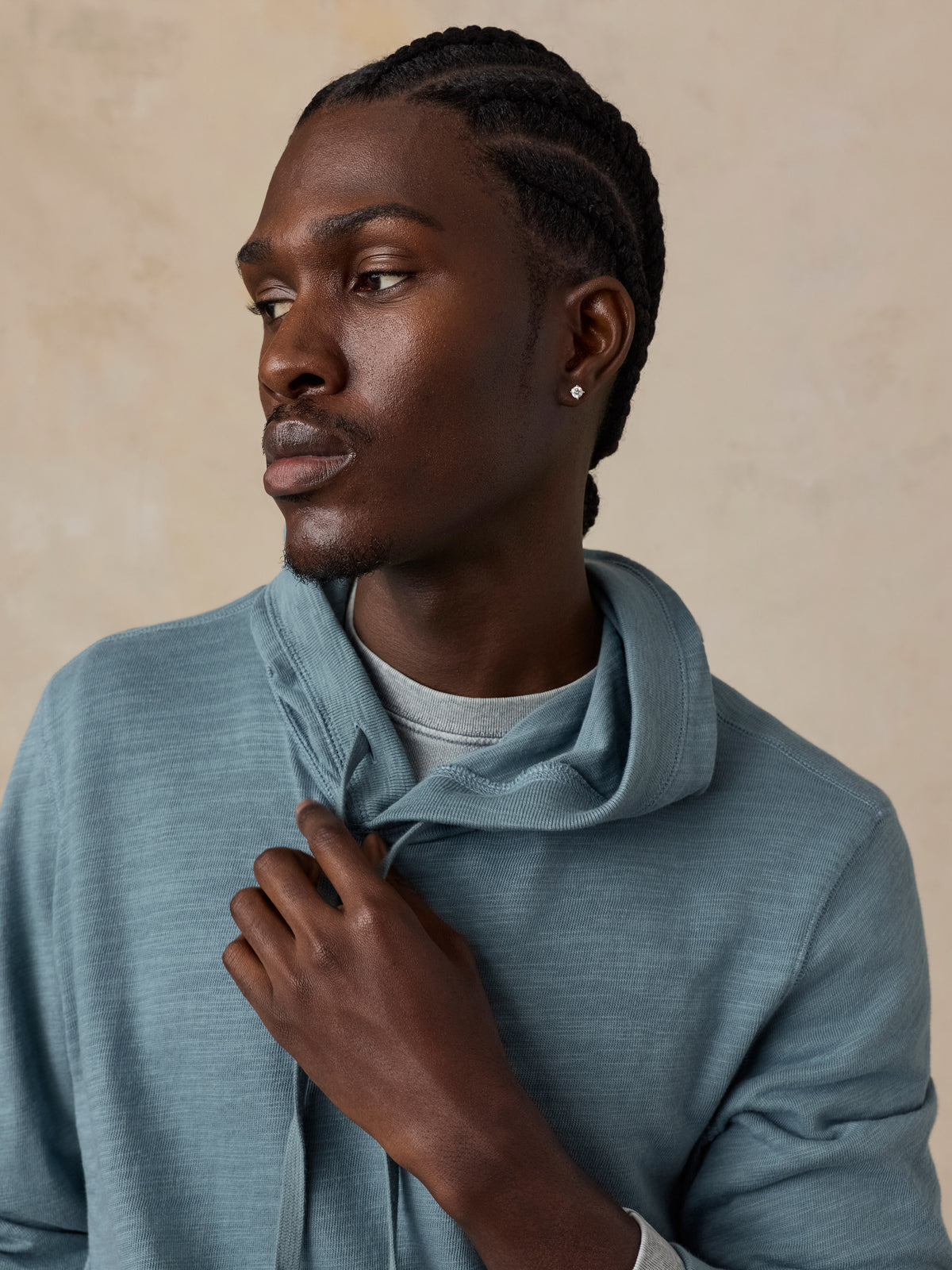 A man wearing a dusty blue-gray hooded knit sweatshirt over a light gray t-shirt.