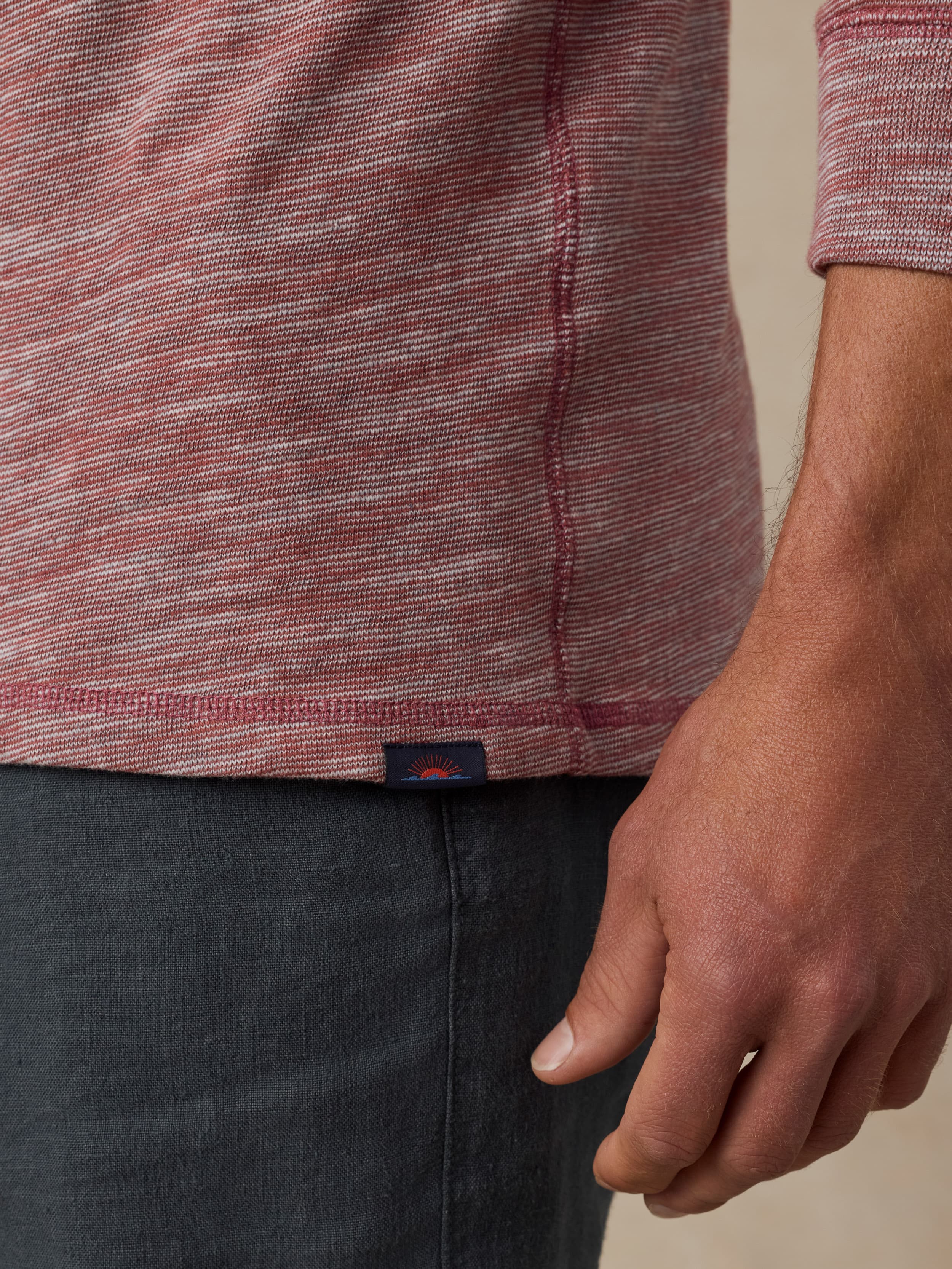 Close up of a man wearing a red heathered hoodie with a visible Faherty brand label and black shorts against a beige background