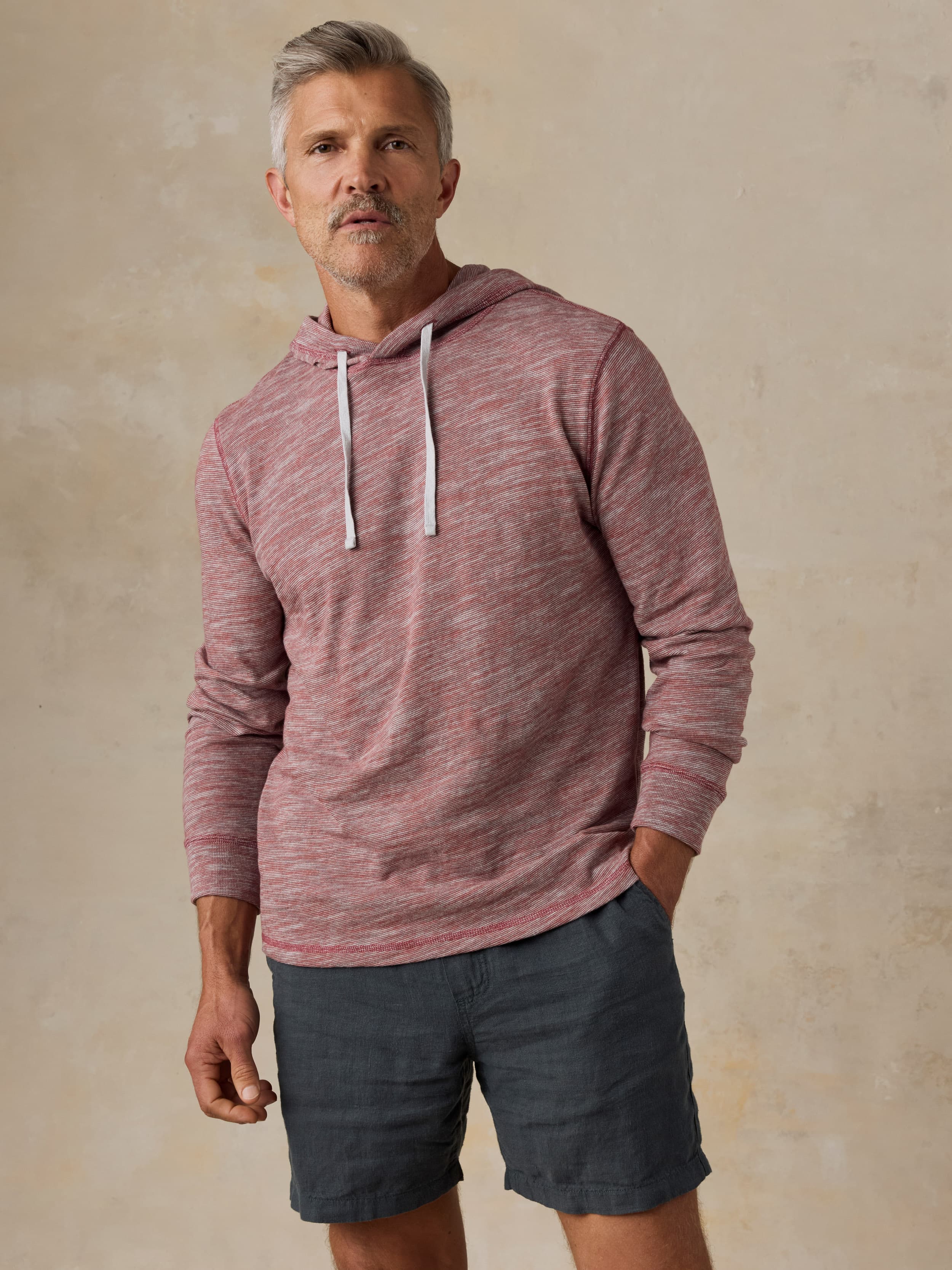 Man wearing a red heathered hoodie and black shorts against a beige background