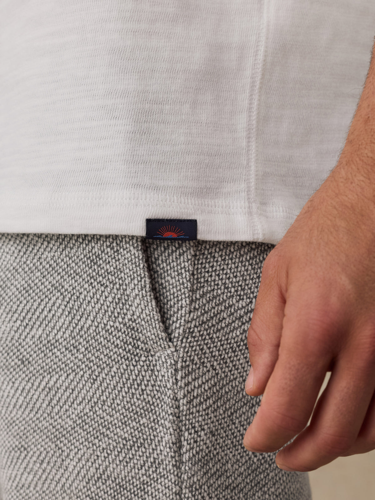 Close-up of a person wearing a white ribbed knit hoodie and textured gray herringbone sweatpants, with a small dark Faherty brand tab visible at the hem., image 3 of 8