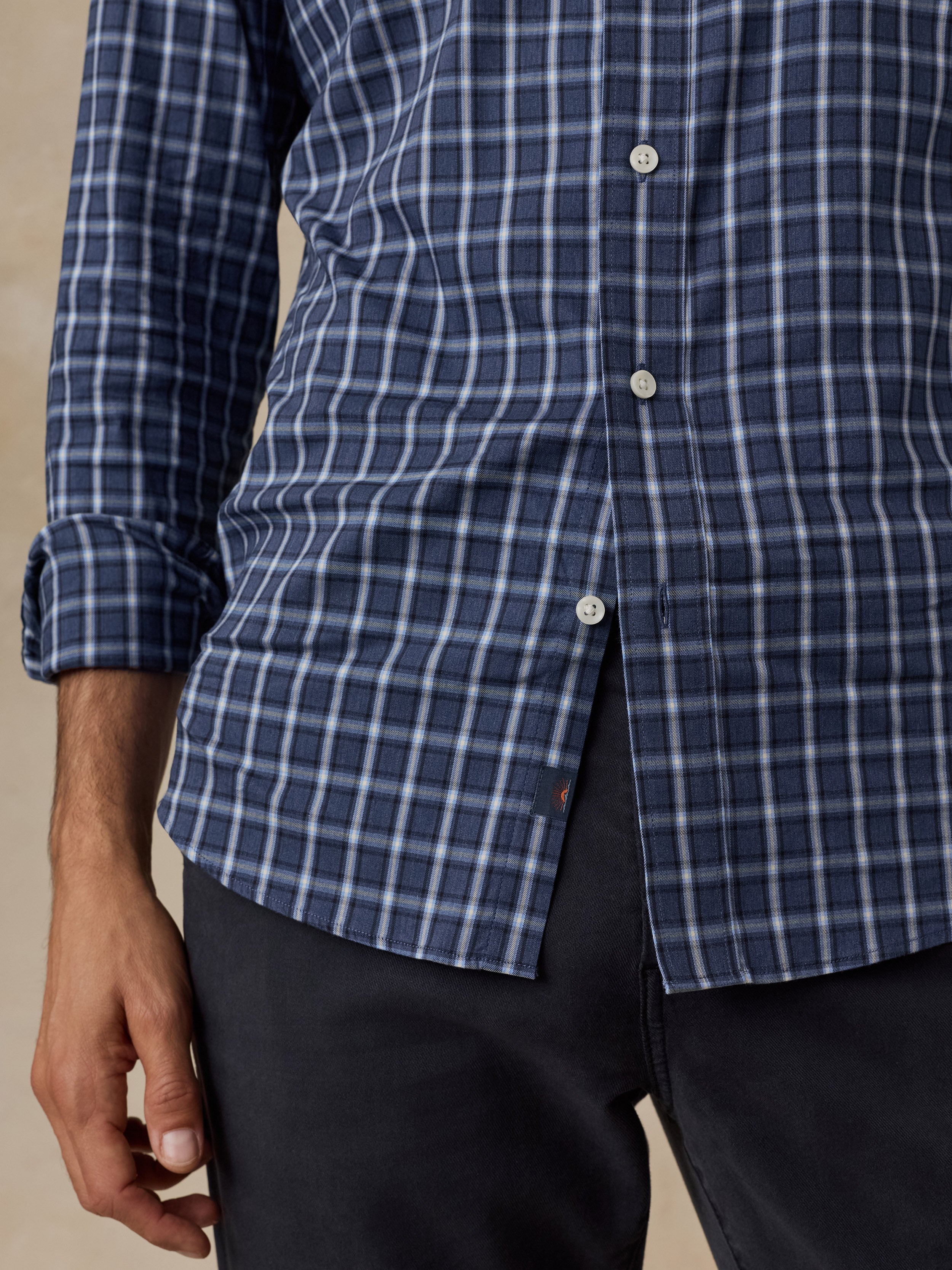 A close-up of a man wearing a blue and white plaid button-down shirt with dark trousers, cropped from the chest down.