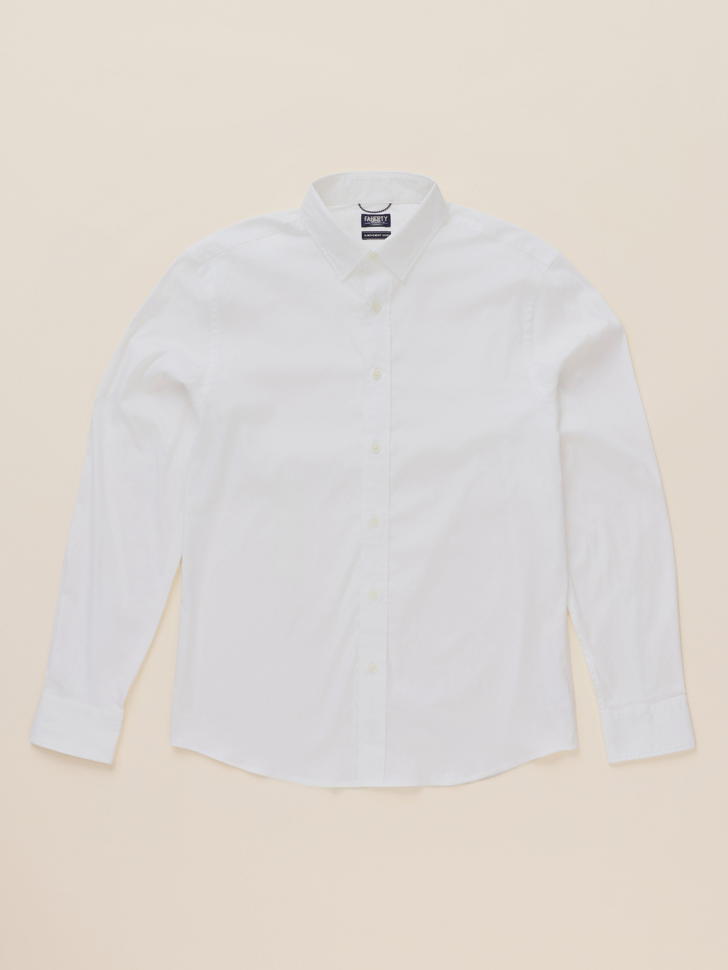 A white long-sleeve button-down shirt with a classic collar, laid flat against a solid, warm beige background.