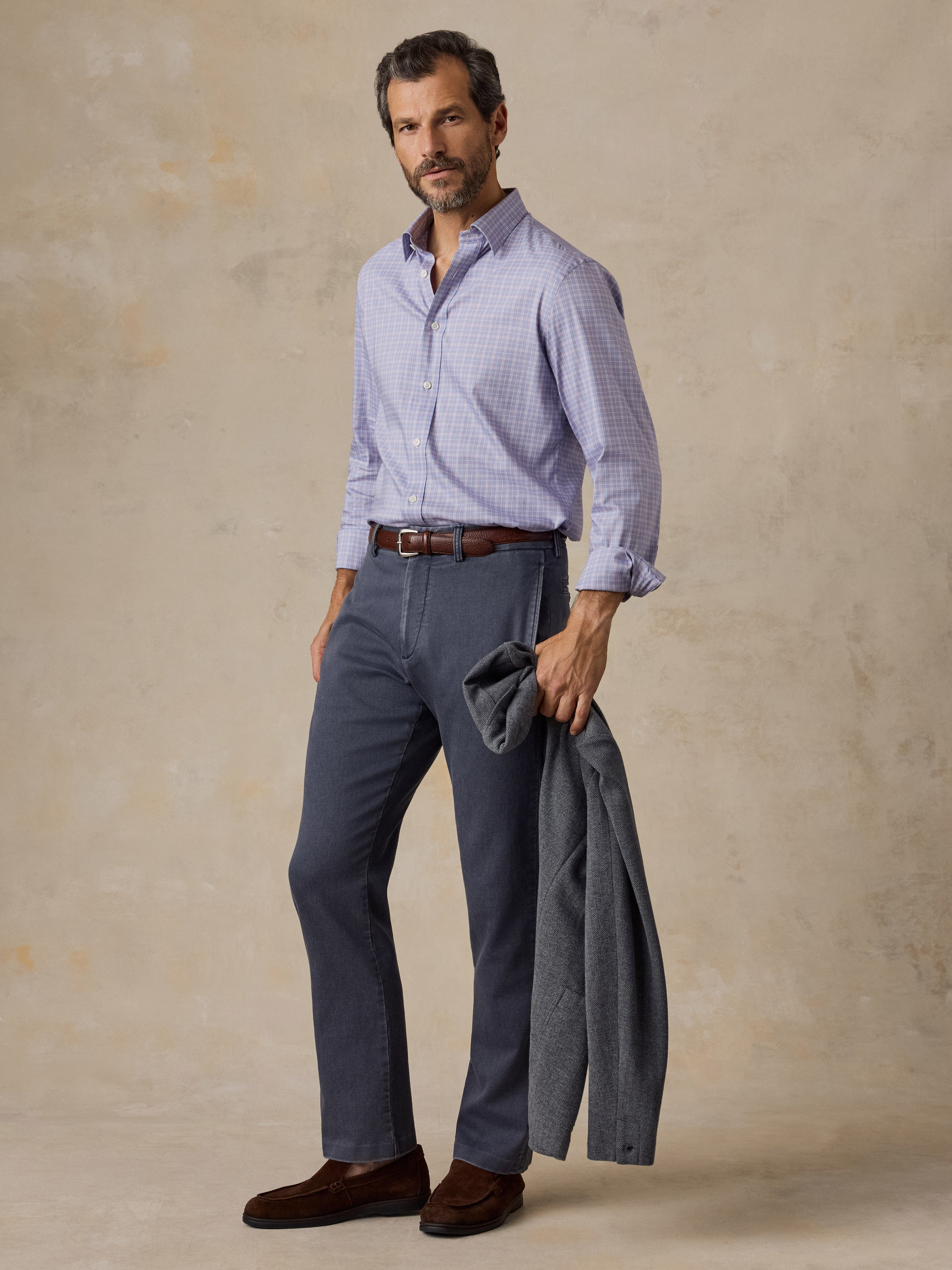 Man wearing a light purple plaid shirt, dark grey chino pants, and a grey blazer