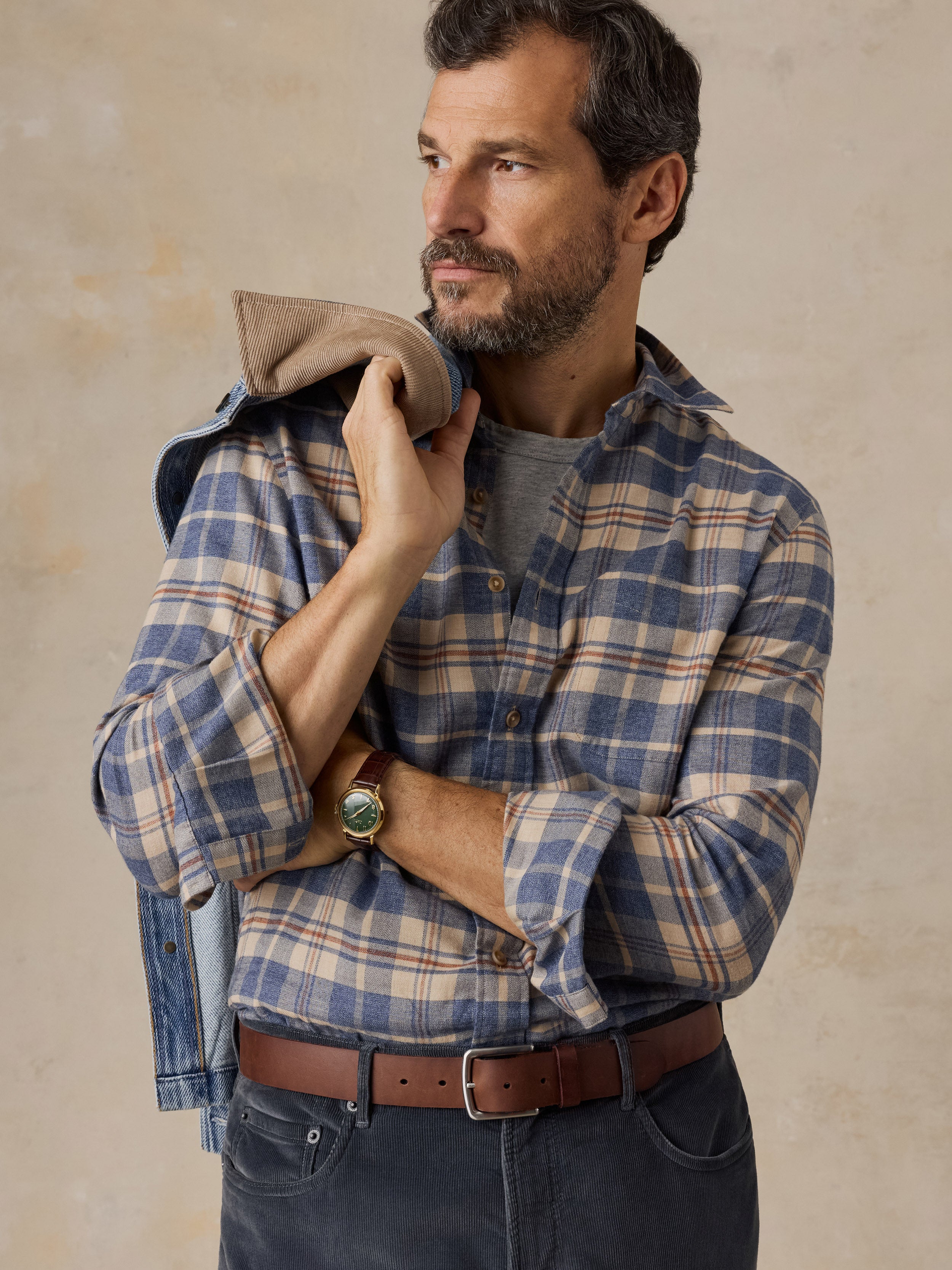 A close up of a man wearing a blue and beige plaid shirt and dark pants