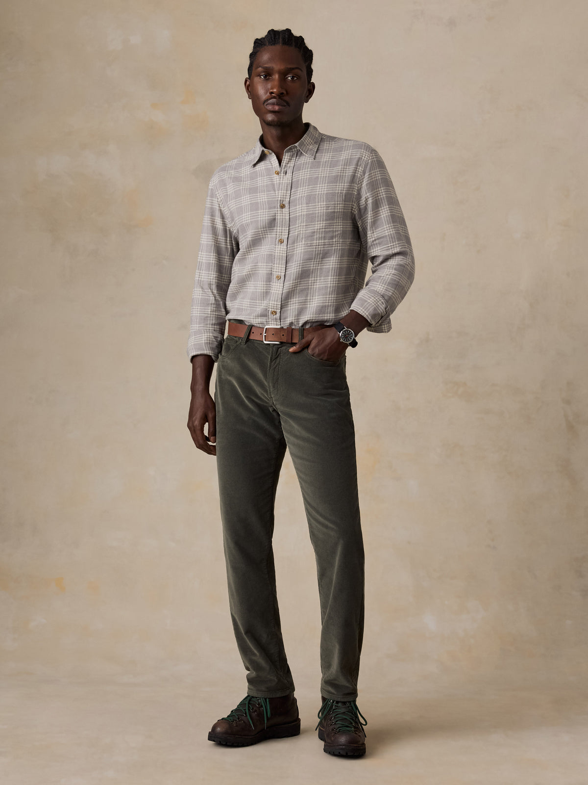 A man wearing a grey plaid button up shirt and green corduroy pants, image 3 of 5