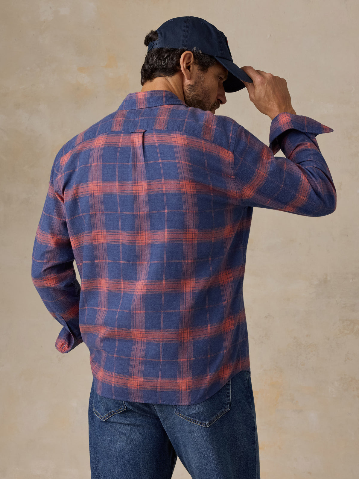 A man viewed from behind wearing a blue plaid shirt, blue jeans, and a hat, image 4 of 5