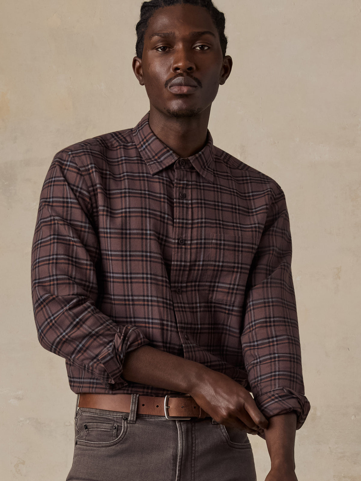 A man wearing a red plaid shirt and brown pants, image 4 of 5