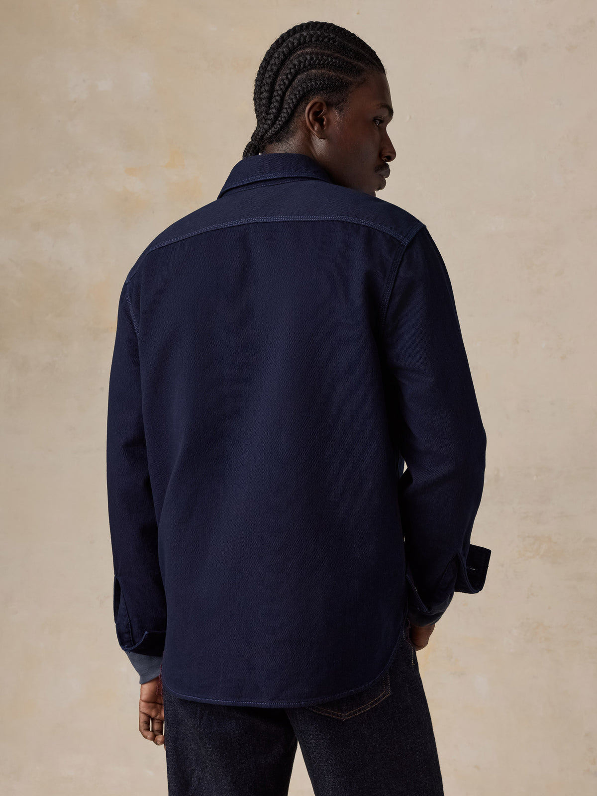 A man viewed from behind wearing a blue workshirt and blue jeans, image 5 of 6