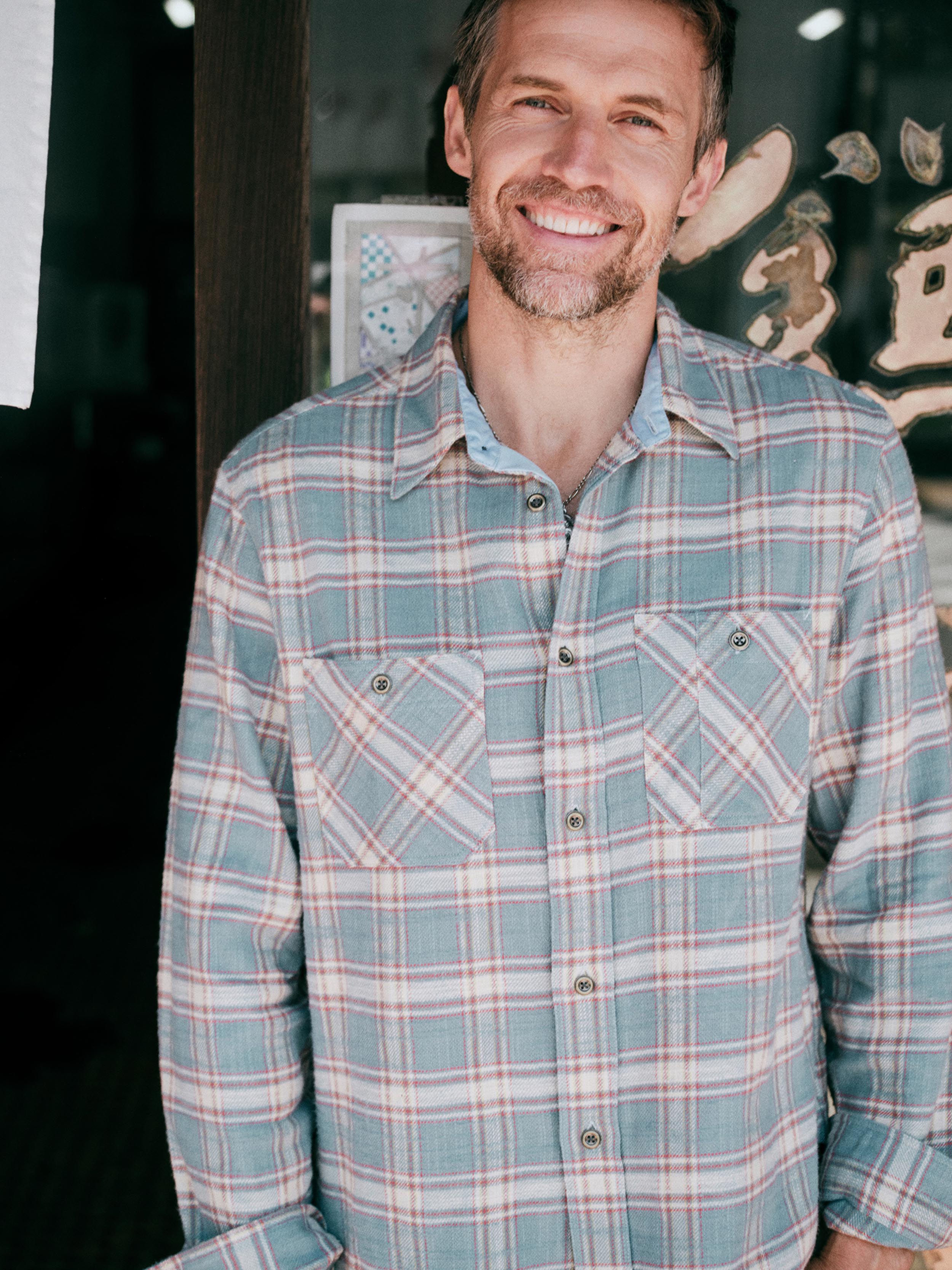 A man wearing a long-sleeve plaid button-up shirt in muted blue, beige, and red tones