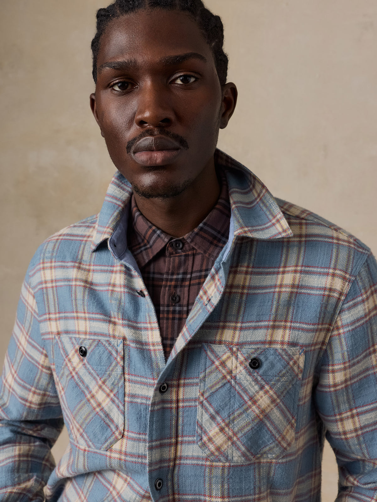 Close up of a man wearing a light blue plaid shirt over a plaid button up , image 6 of 7