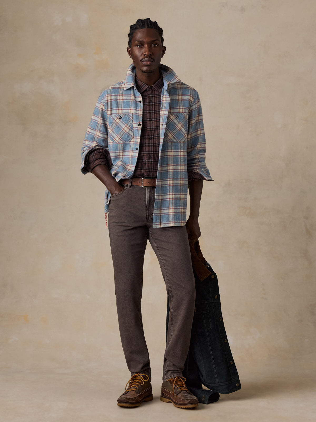 A man wearing a light blue plaid shirt over a plaid button up with brown pants, image 7 of 7