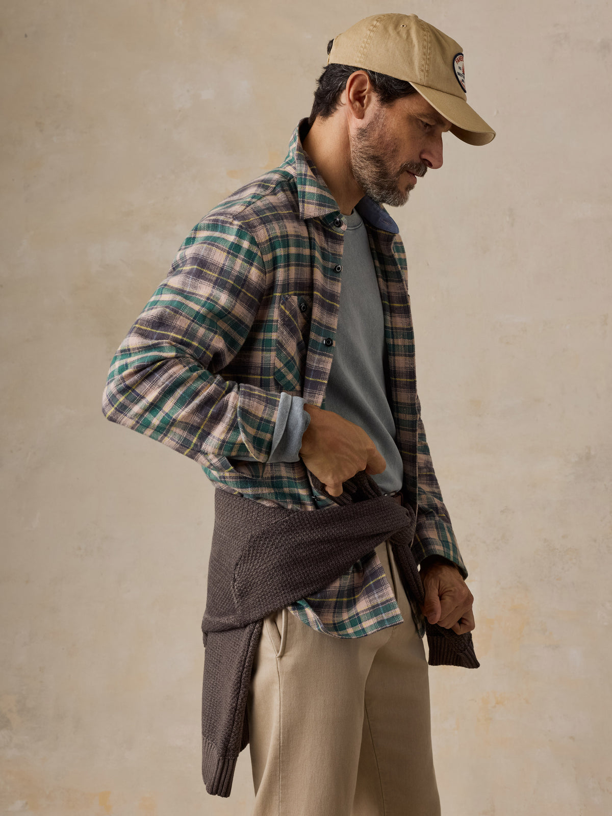A man wearing a green flannel over a green shirt with beige pants and a hat, image 4 of 5
