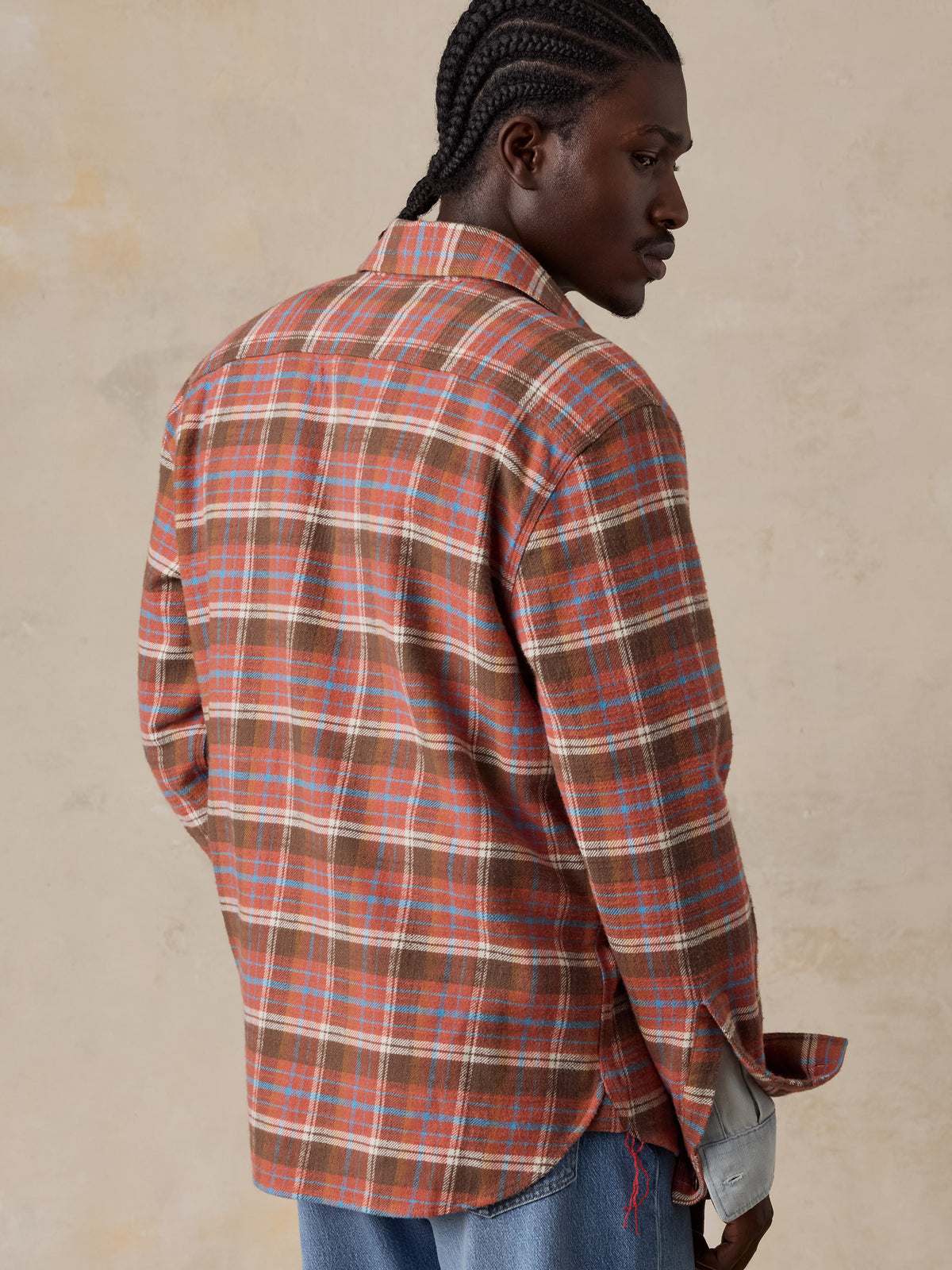A man viewed from behind wearing a red plaid flannel over a chambray shirt and blue jeans, image 3 of 5