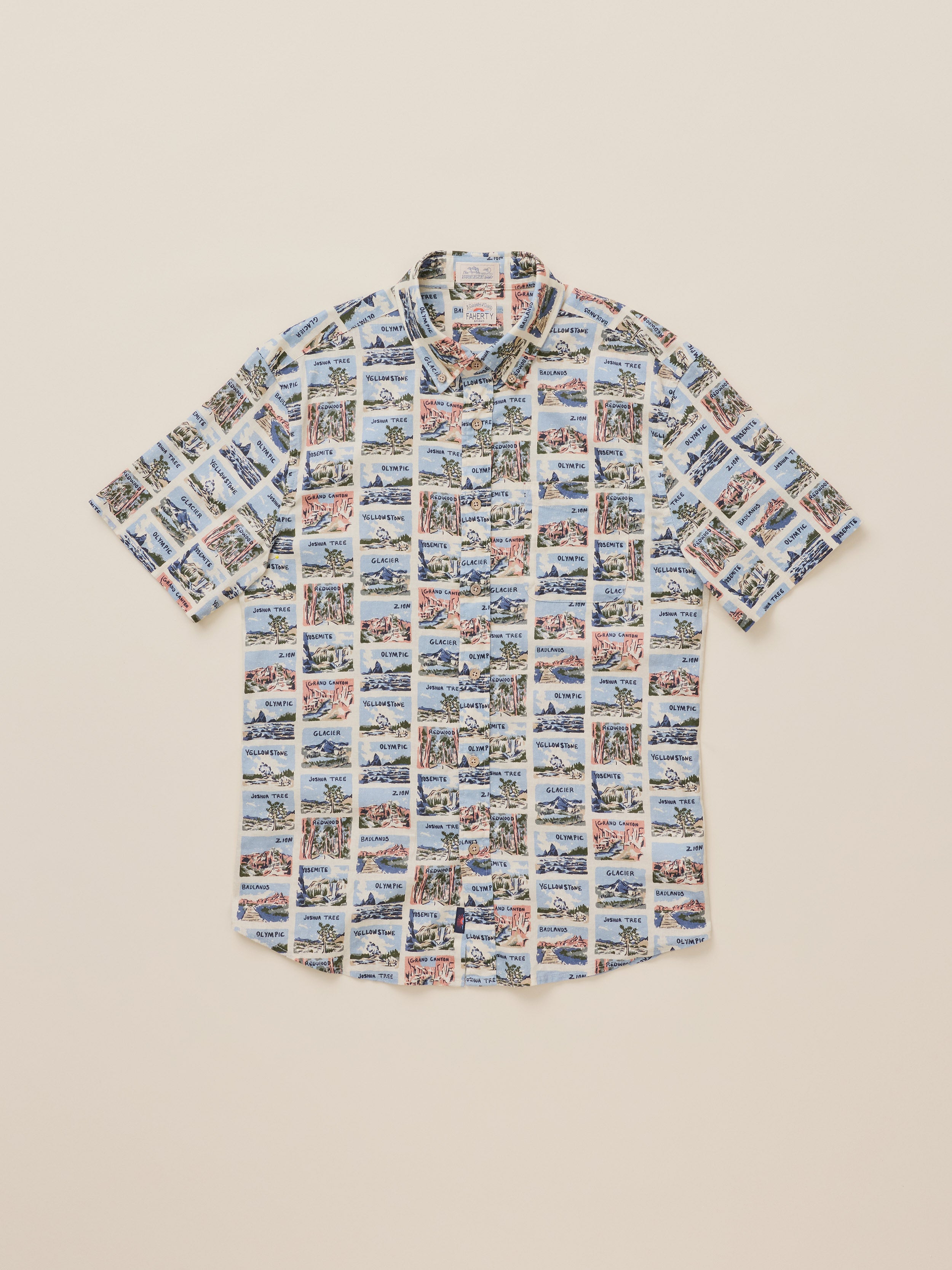 A short-sleeve button-up shirt with an all-over collage print of National Park scenes, laid flat on a light beige background.