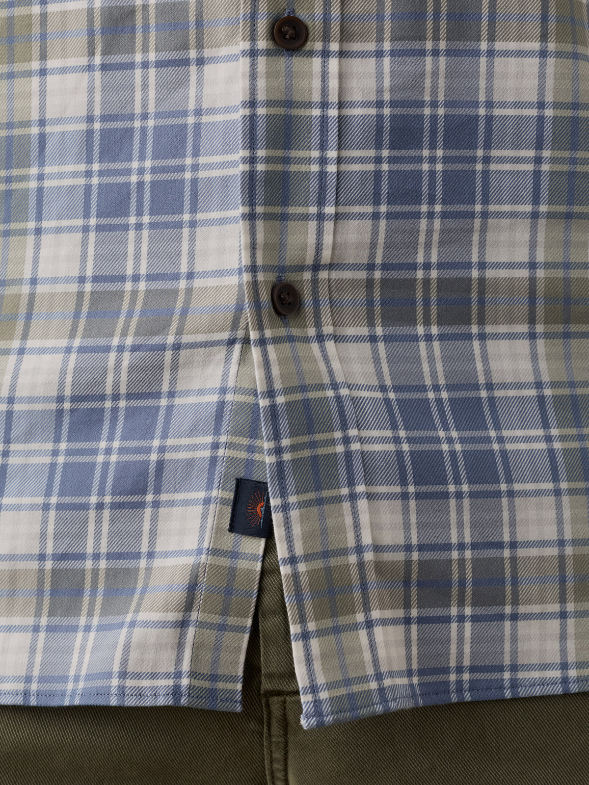 Close-up of a plaid button-up shirt in blue, white, and gray, with dark buttons and a small Faherty brand tag near the hem., image 4 of 6