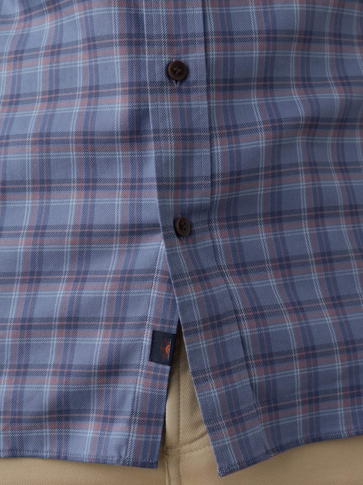 Close-up of a plaid button-down shirt in blue, red, and white, with dark brown buttons and a small Faherty brand tag near the hem., image 5 of 6