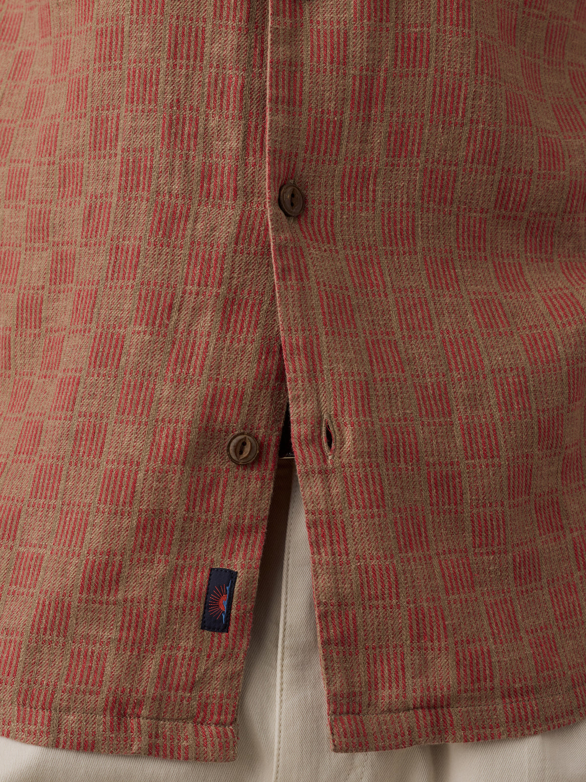 Close-up of a textured woven shirt fabric with a red and beige basketweave pattern, featuring brown buttons and a small Faherty brand tag., image 7 of 7