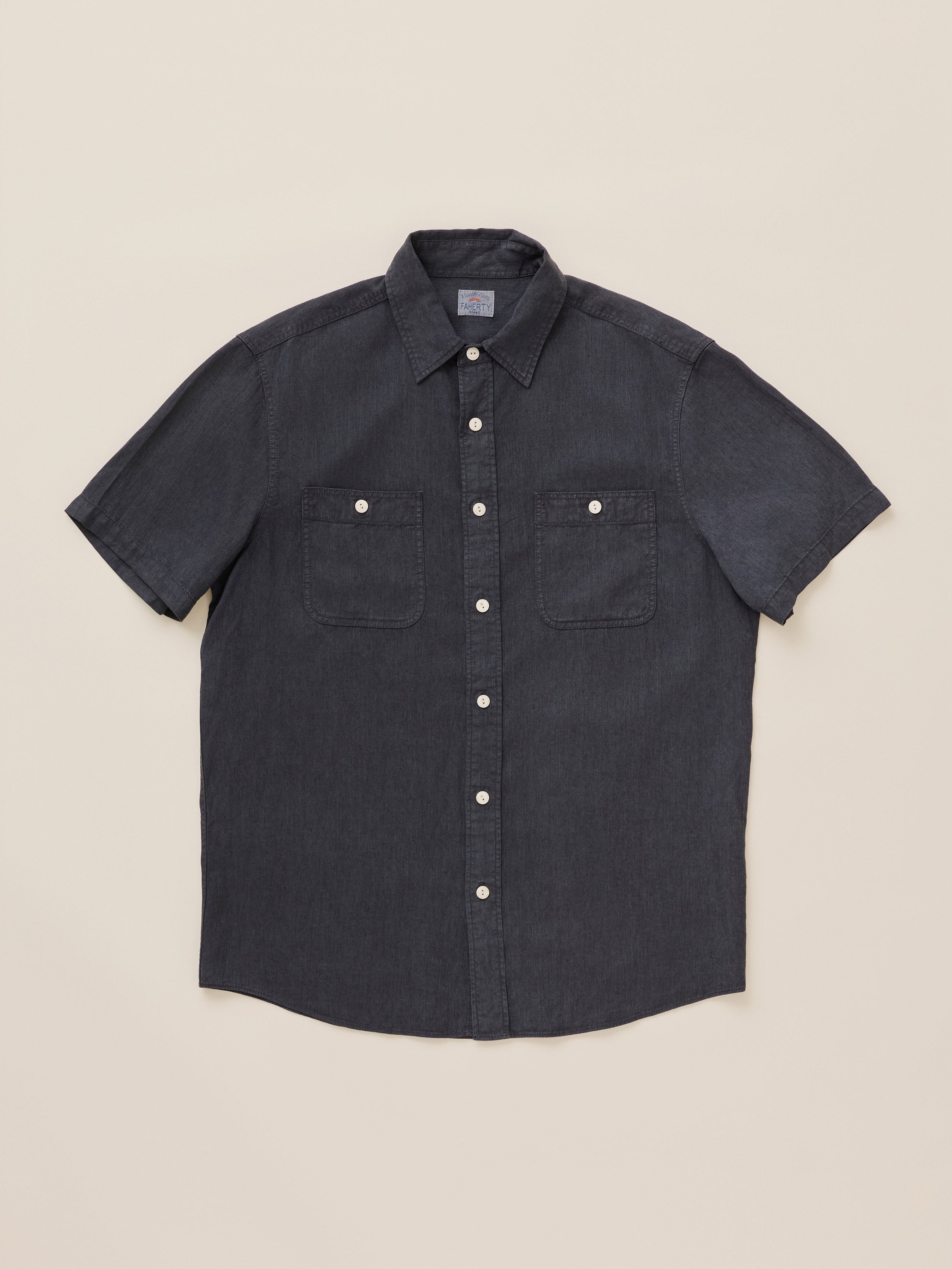 A dark charcoal gray short-sleeve button-up shirt with two chest pockets, laid flat on a light beige background.