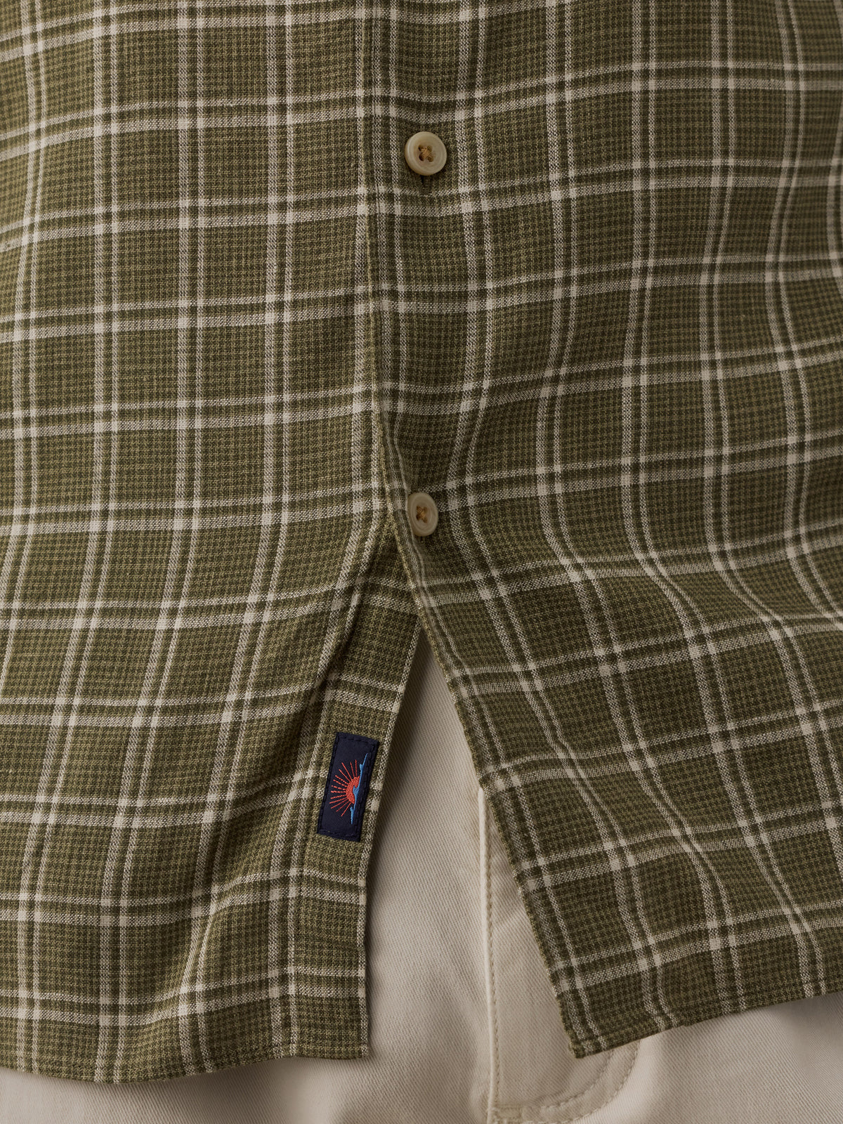 Close-up of a plaid button-up shirt in olive green and white, showing the front buttons and a small Faherty brand tag near the hem. , image 4 of 6
